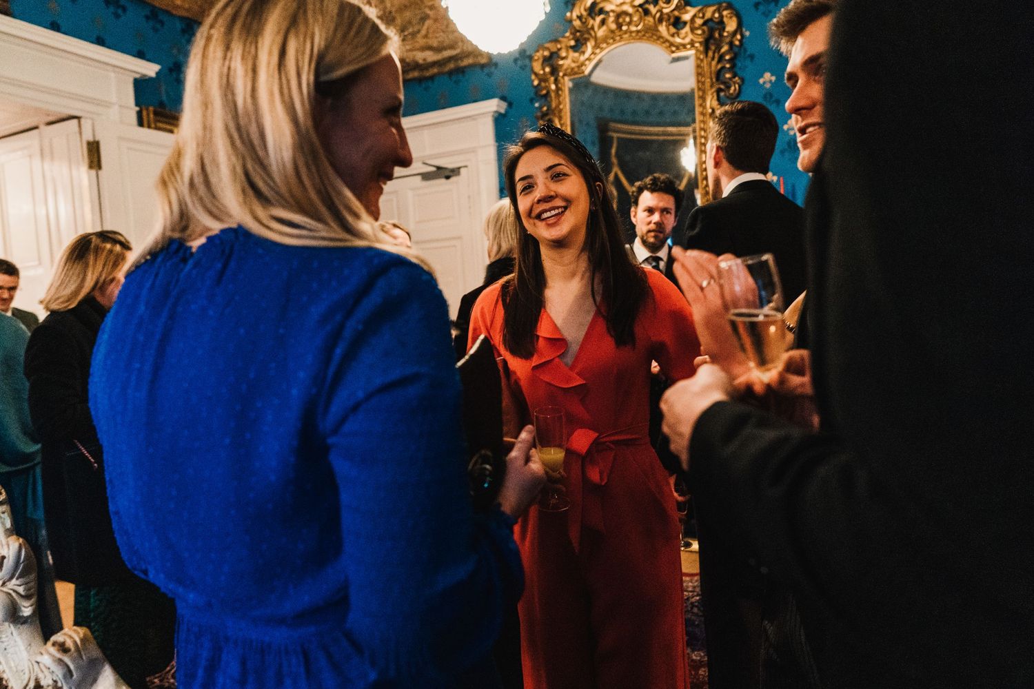 Wedding guests in colorful attire socialize and share drinks at an elegant indoor reception.