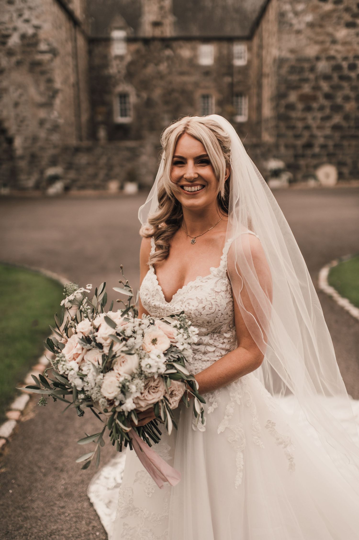 Close-up bridal portrait featuring an elegant white dress and romantic bouquet against stone architecture.