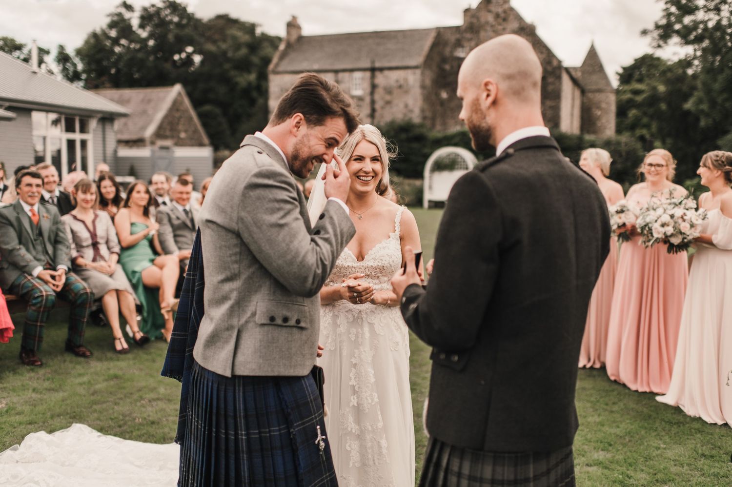 An outdoor wedding ceremony with attendees in traditional Scottish attire.