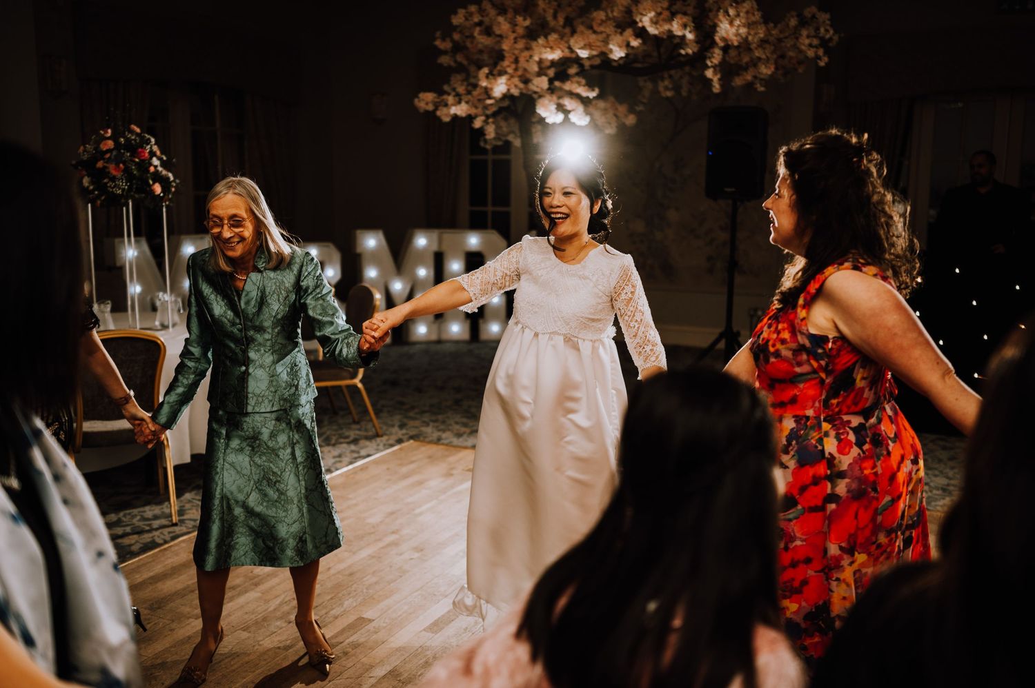 Wedding guests dance joyfully together on a reception dance floor decorated with string lights.