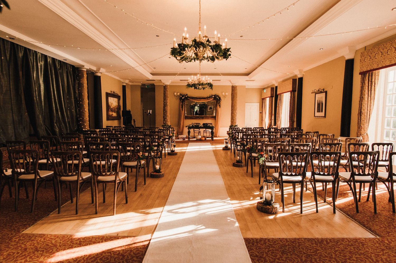Elegant wedding ceremony setup with rows of dark chairs and white aisle runner in a grand ballroom.
