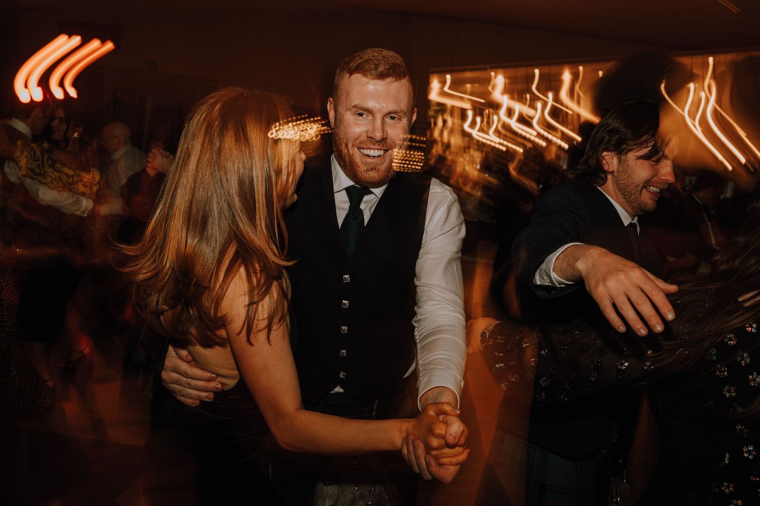 Guests dance together at a reception with warm ambient lighting and motion blur effects.