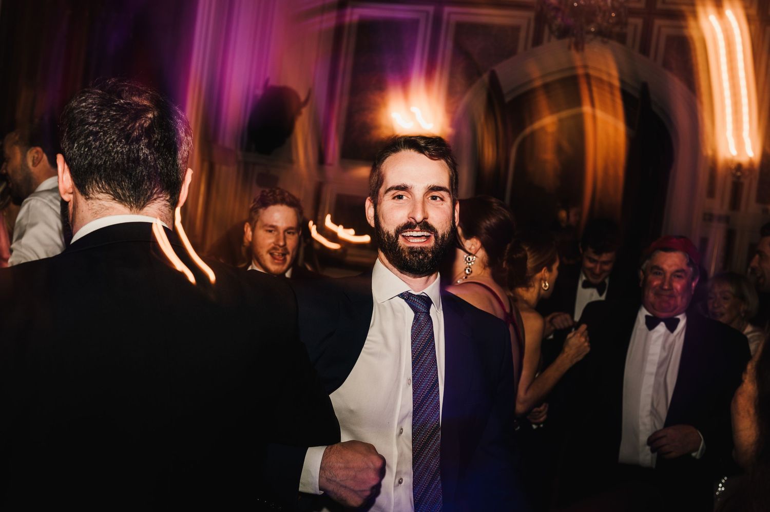 A guest in formal attire smiling at an evening wedding reception.