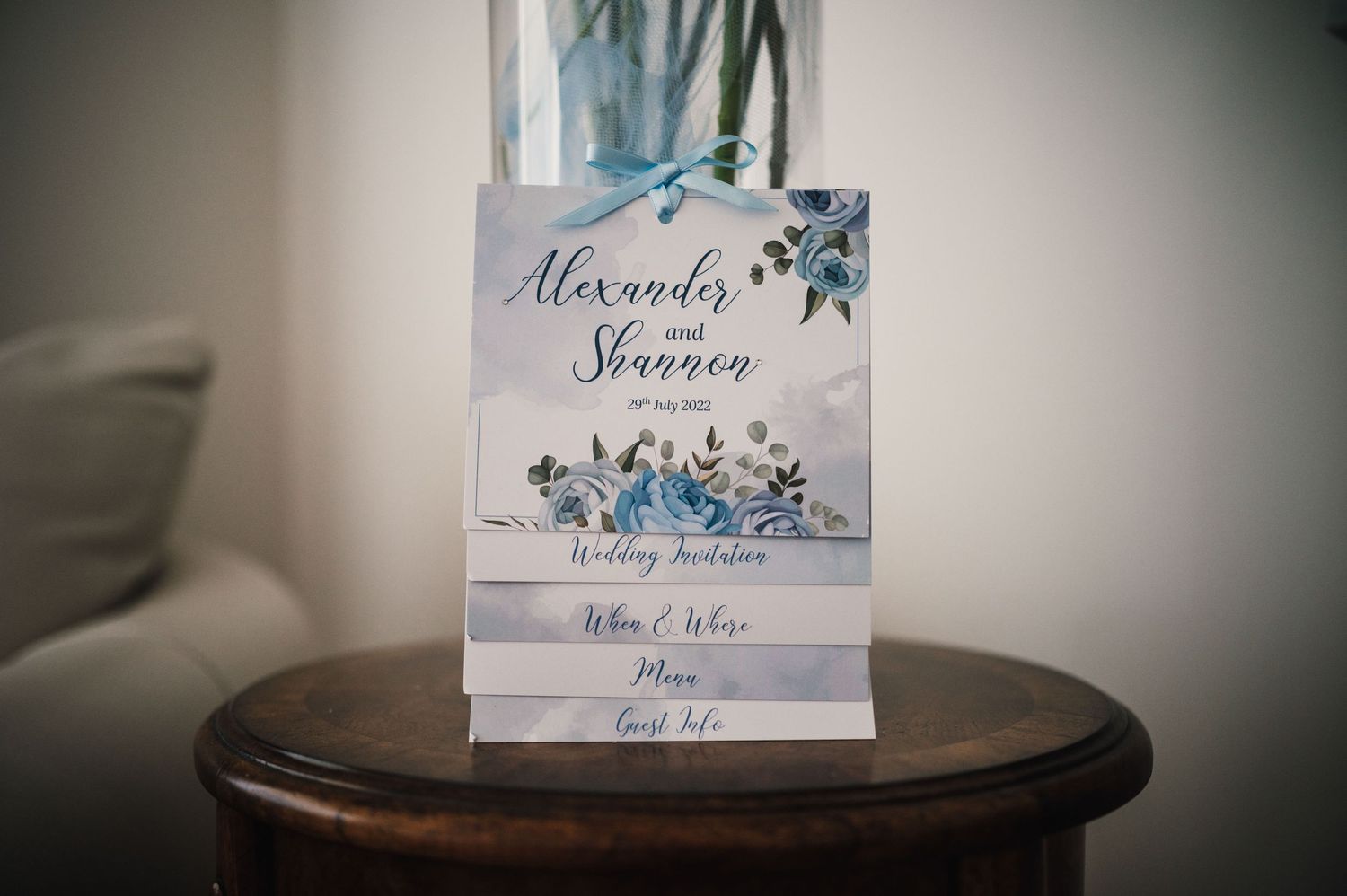 Wedding invitation with blue floral design and elegant typography displayed on dark wooden table.