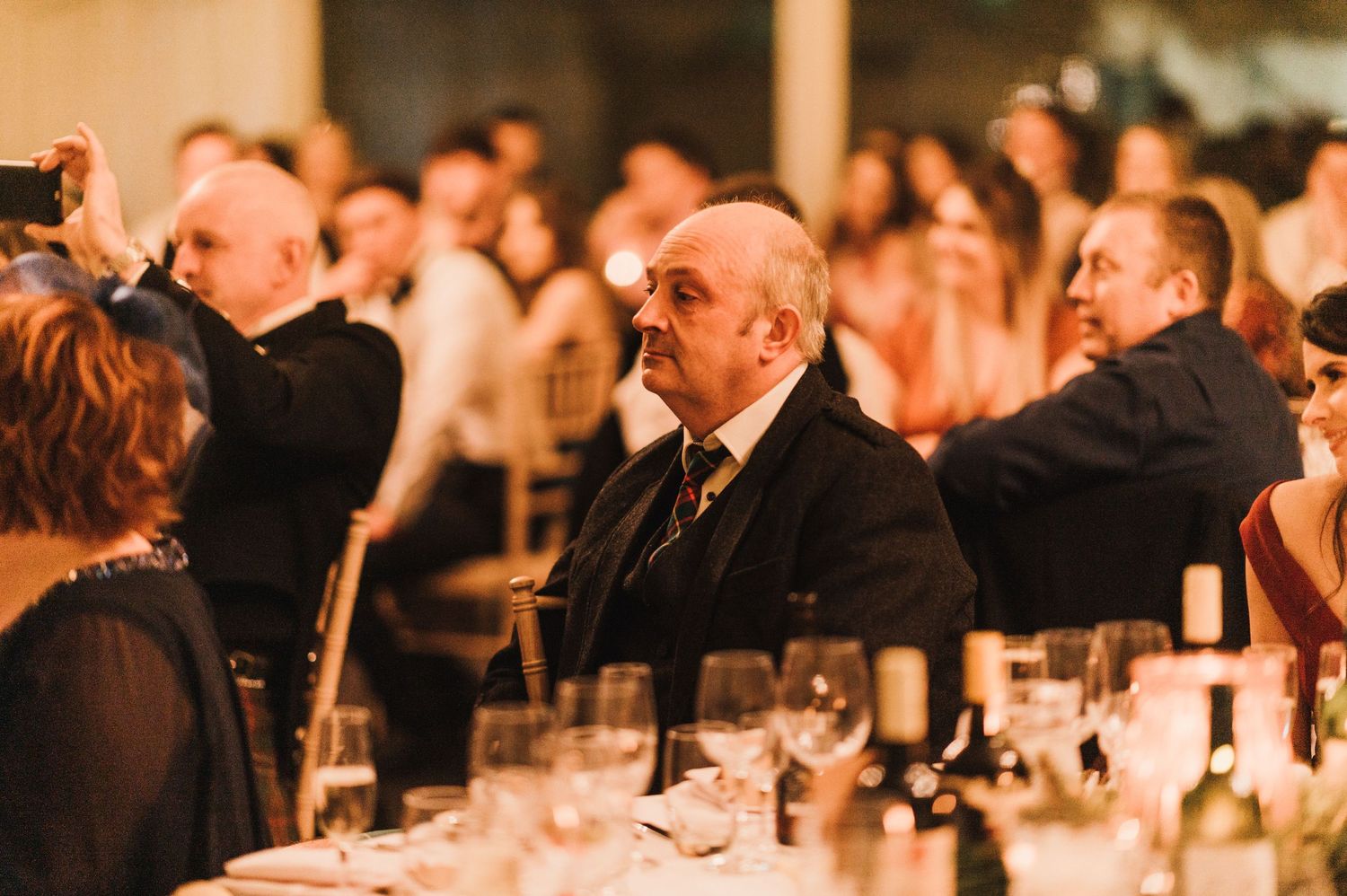 Wedding guests enjoying the reception dinner under warm ambient lighting.