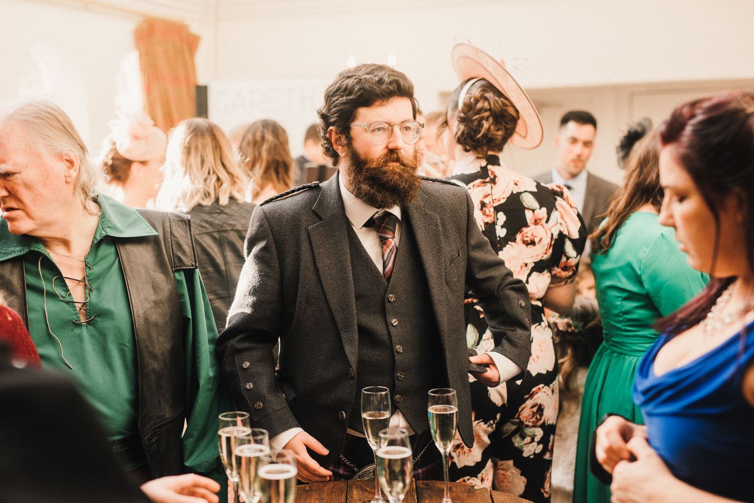 A guest in a dark suit holds a drink during an indoor wedding reception.