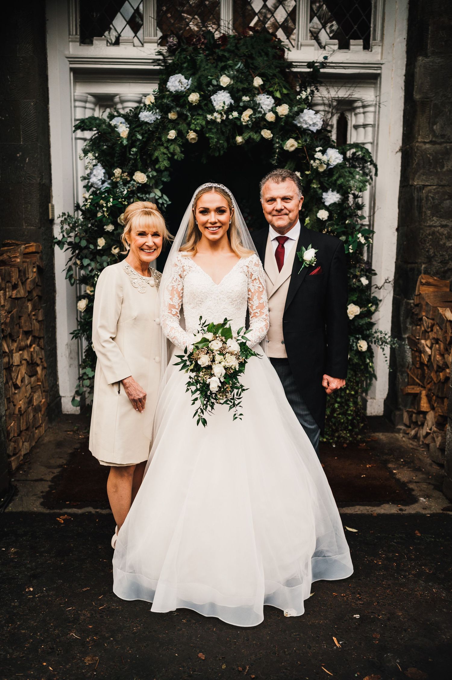 Wedding portrait under an archway decorated with white floral arrangements.