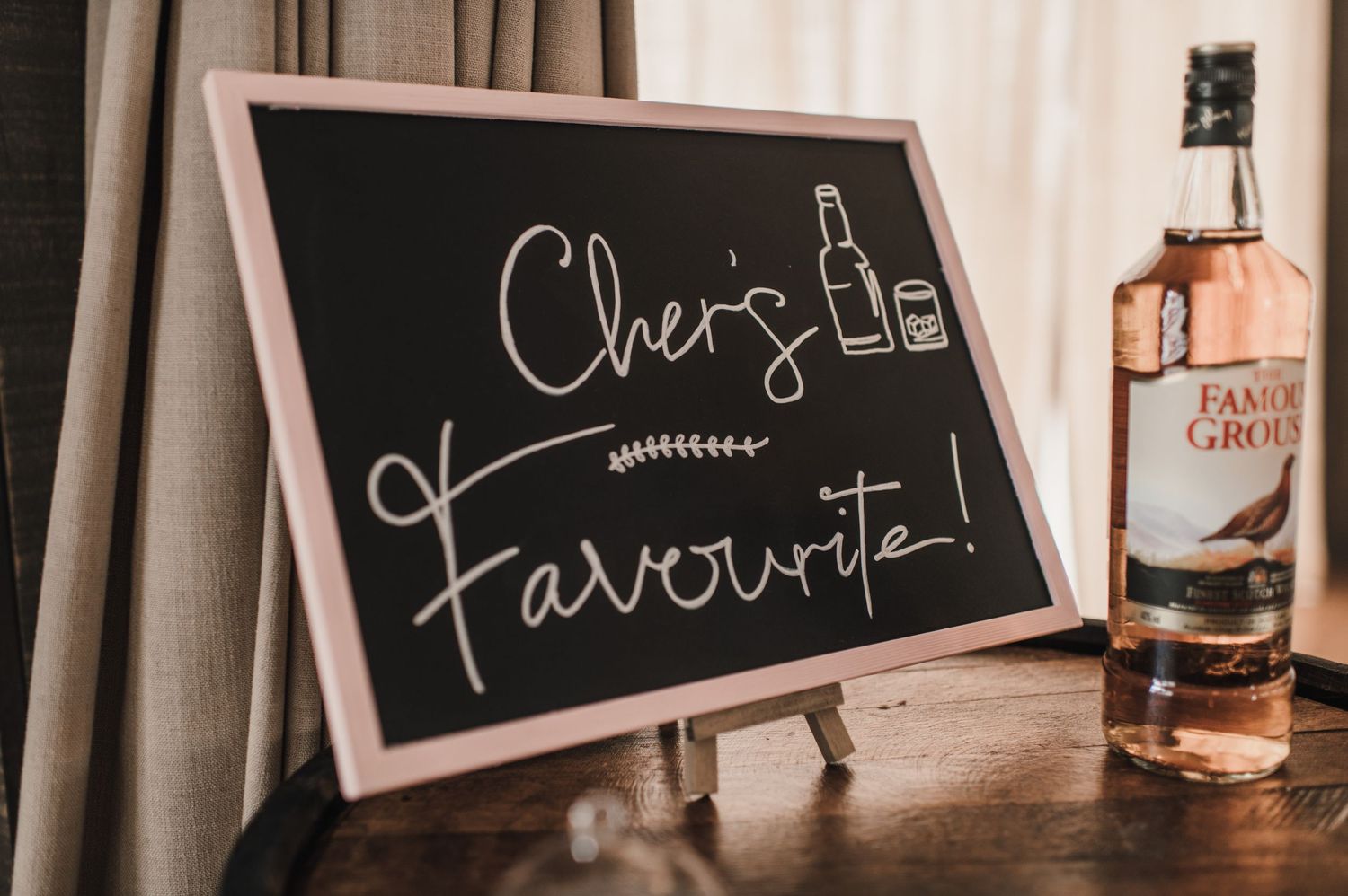 A chalkboard sign displays 'Cheers Favourite' next to a bottle of pink gin.