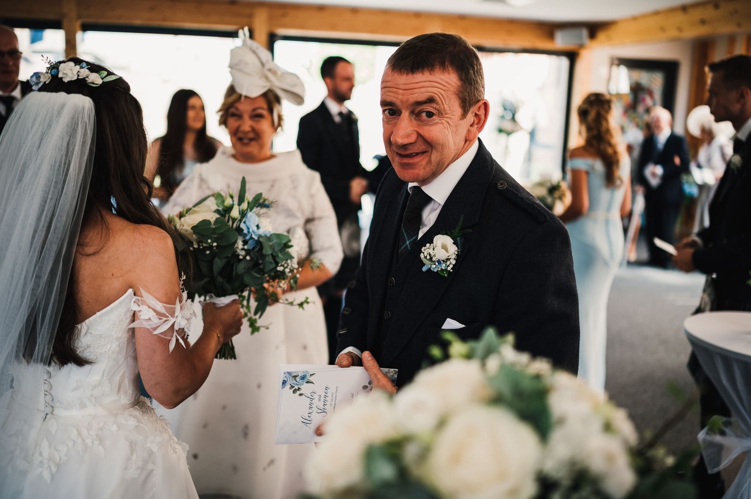 Wedding guests share joyful moments during reception celebration in a rustic indoor venue with wooden accents.