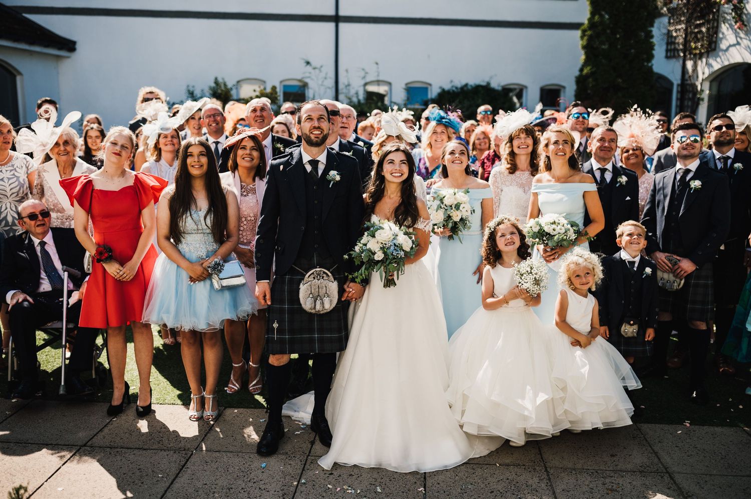 Scottish wedding party group photo with guests wearing traditional kilts and formal attire.