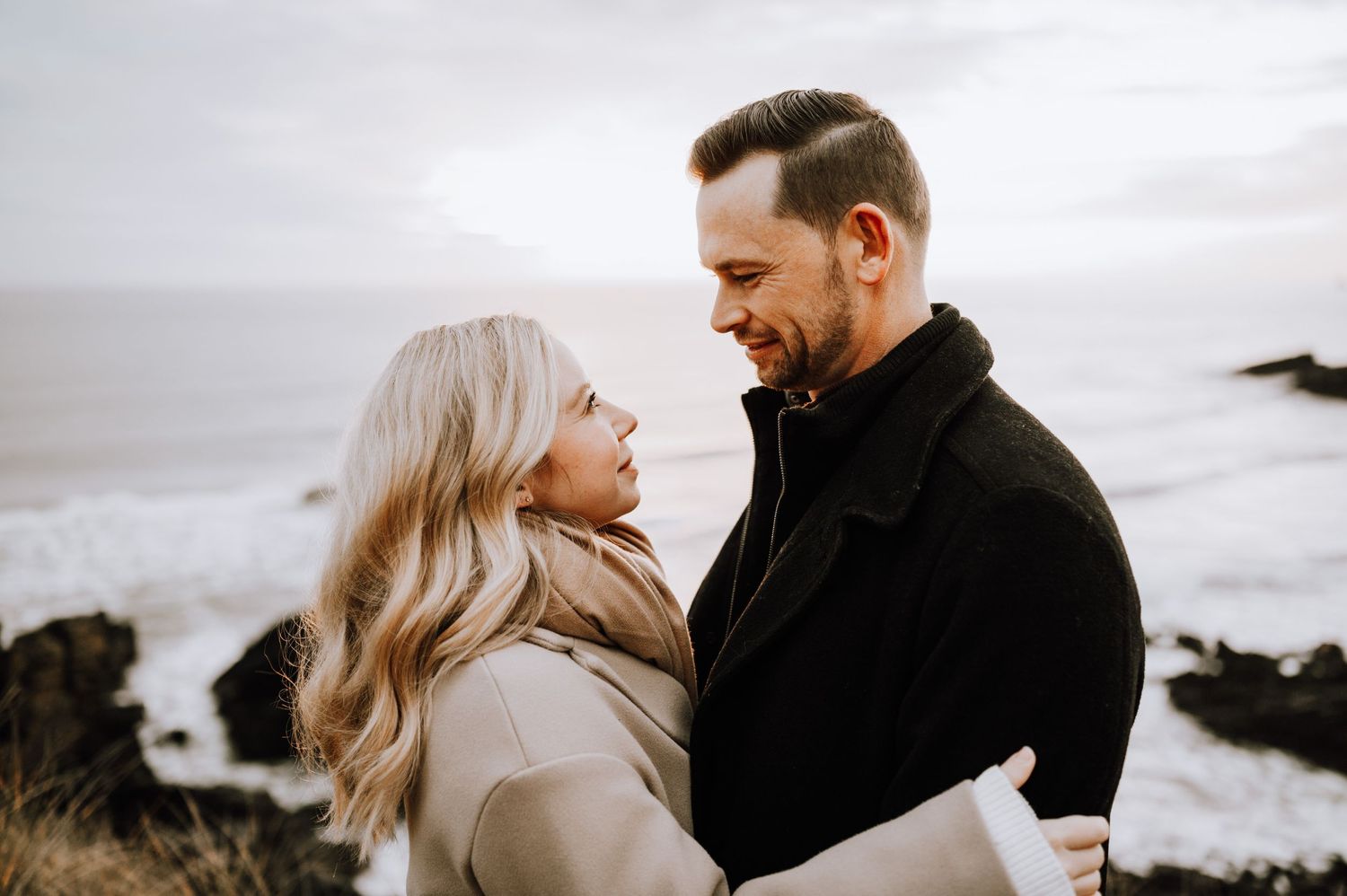 Intimate portrait of a couple in winter coats sharing a moment by the ocean.