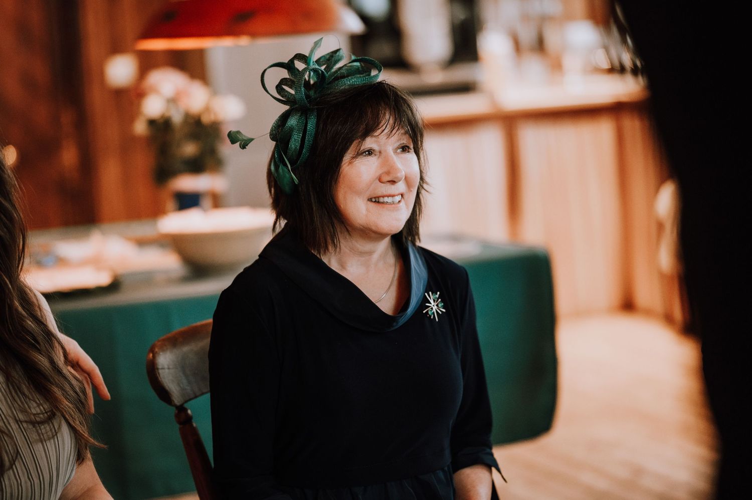 A guest in festive attire smiles during a celebration in a wooden-paneled room.