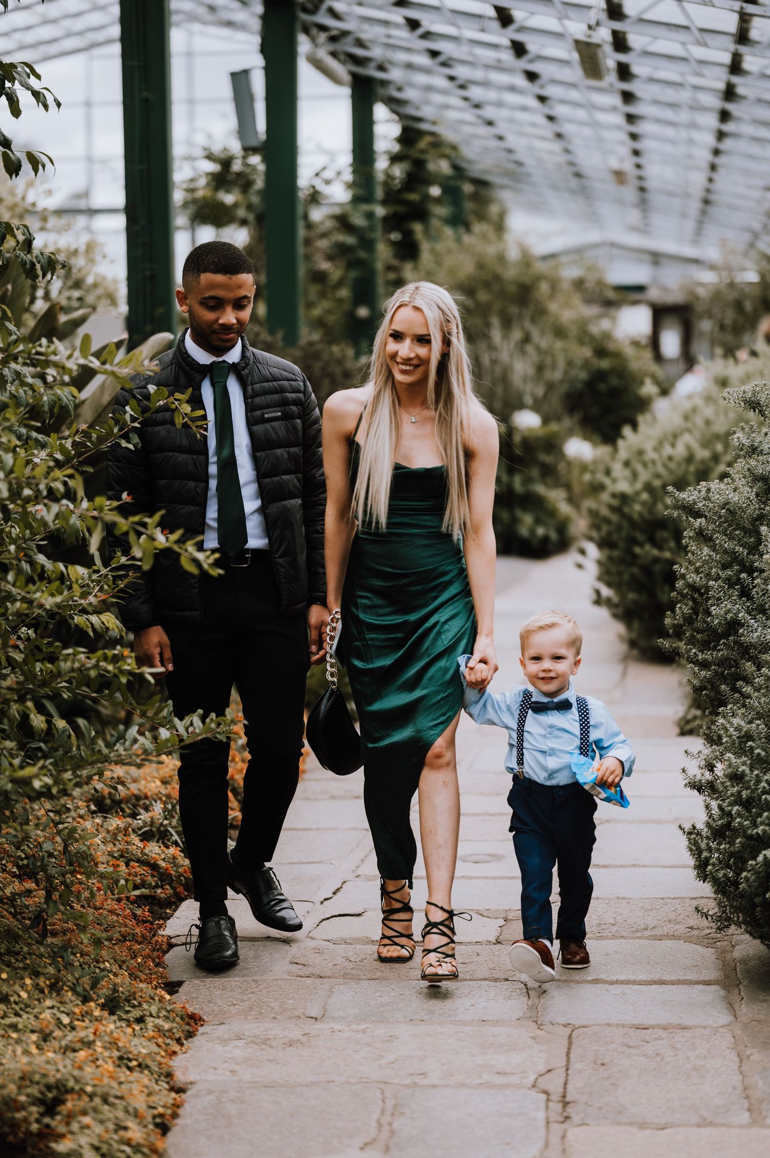 Family walking through a glass-roofed conservatory filled with lush greenery.