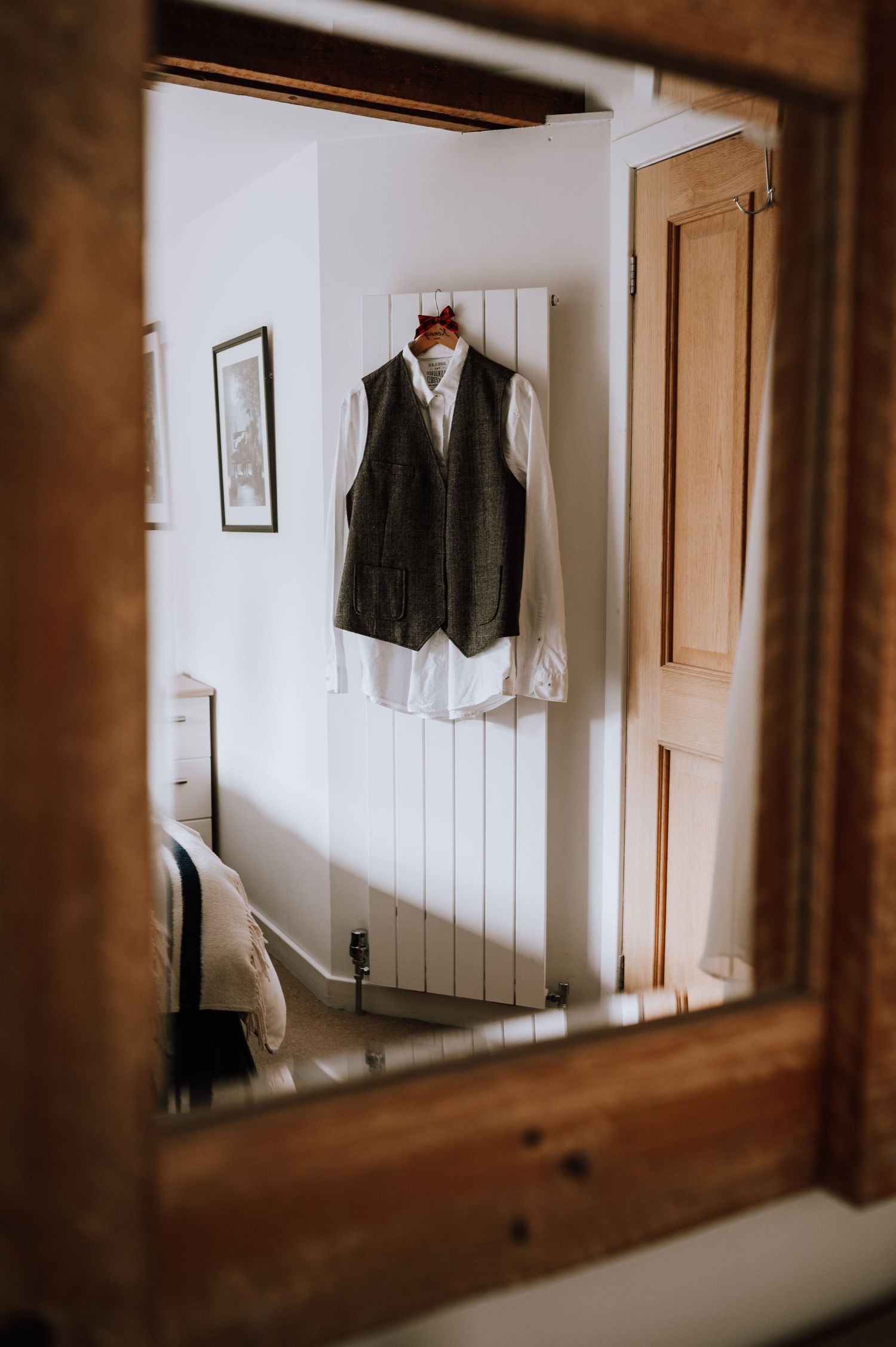 A grey tweed vest and white shirt hanging on a wall, viewed through a wooden mirror frame.