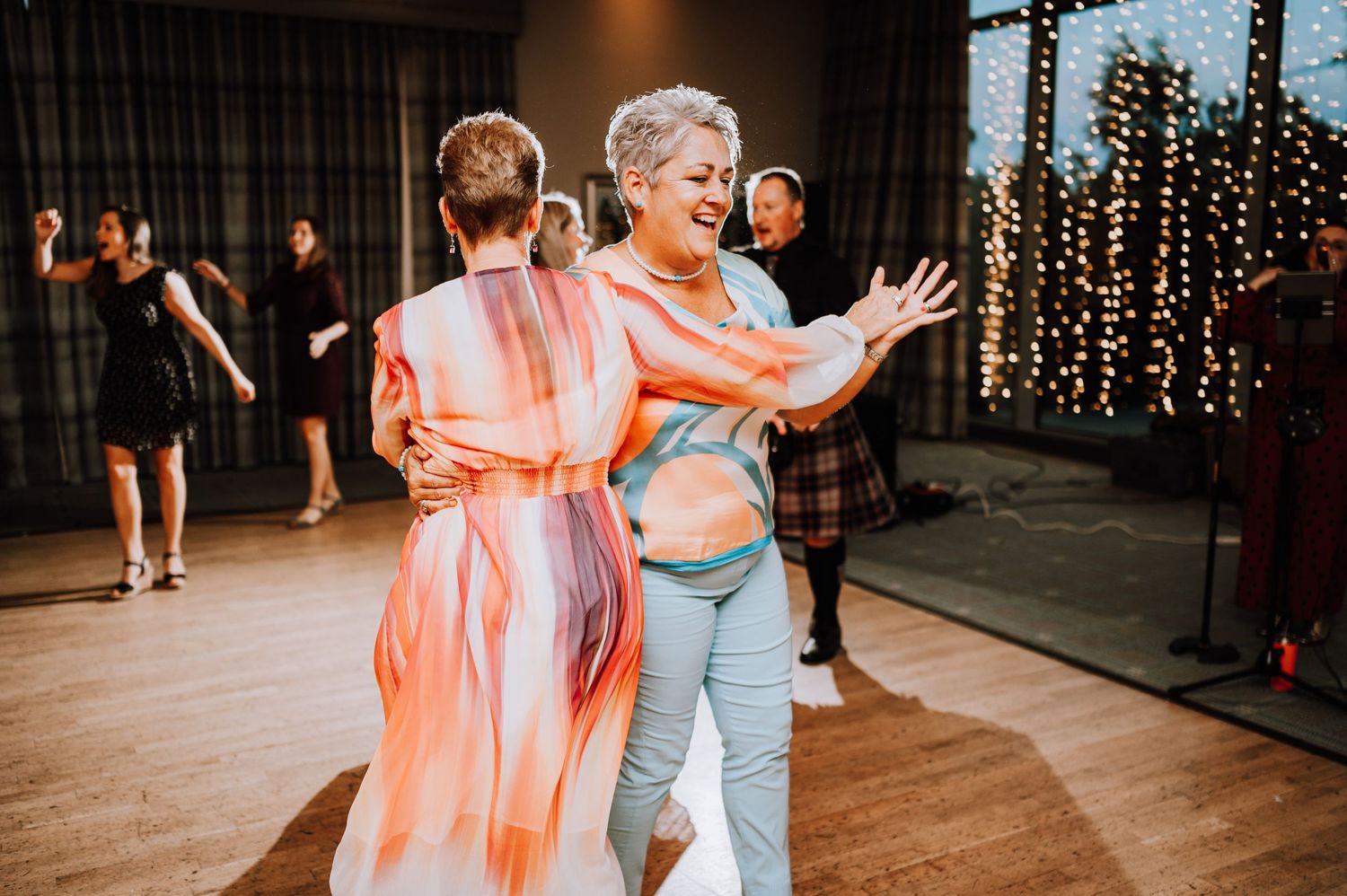 Two people dance together at a wedding reception with string lights decorating the background.