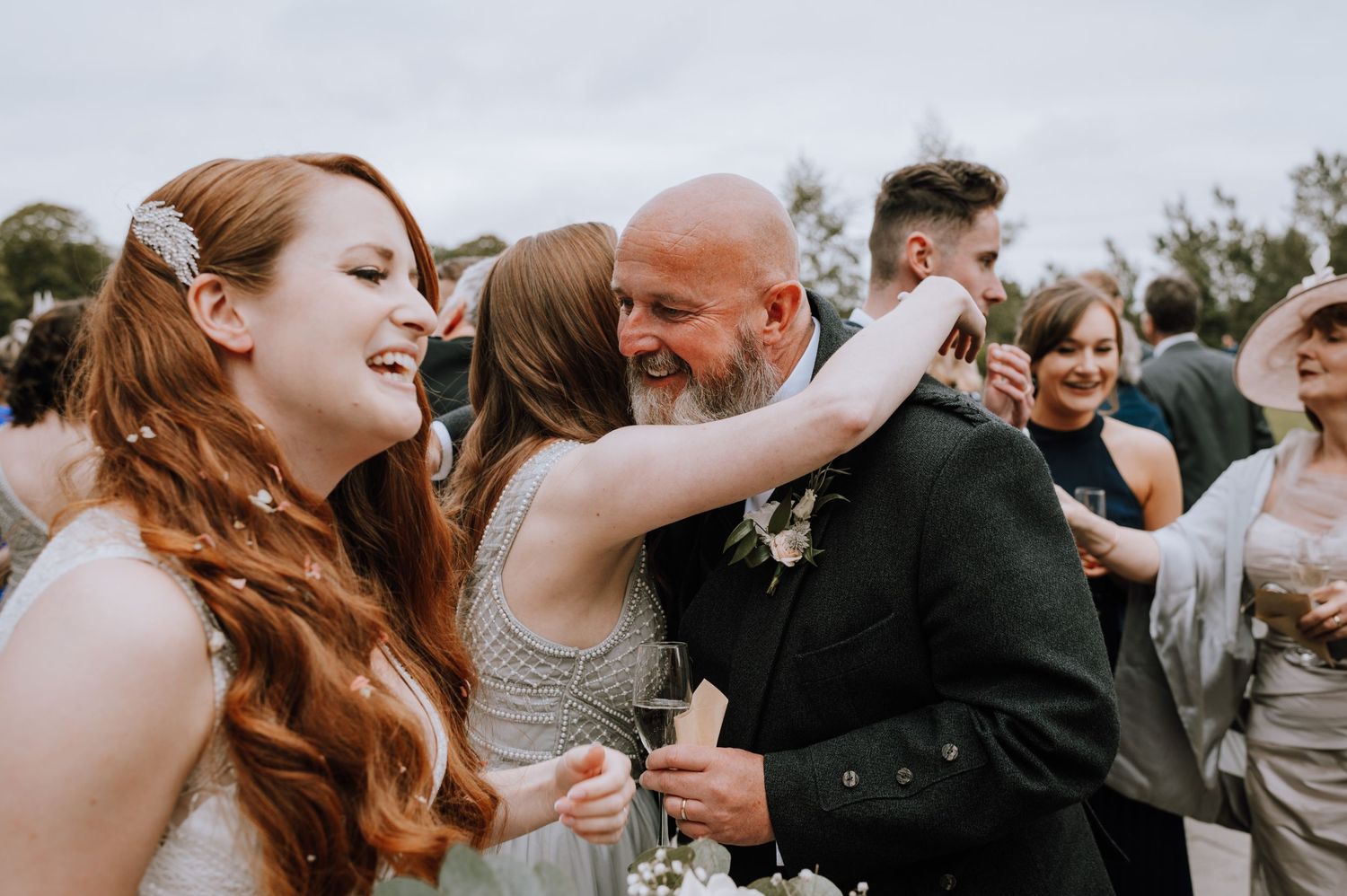 Joyful wedding celebration with guests dancing and embracing outdoors.