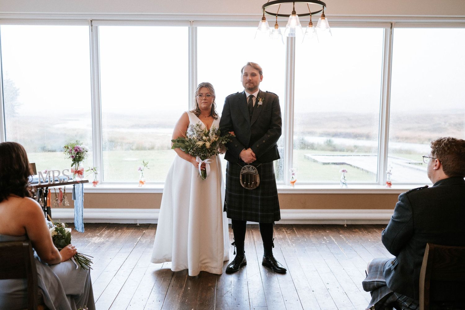 A wedding ceremony in front of large windows overlooking a scenic mountain landscape.