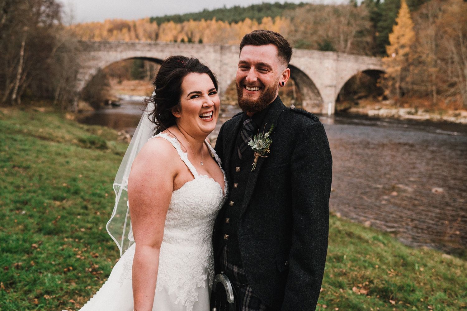 Newlyweds share a joyful moment by a stone bridge on their autumn wedding day.