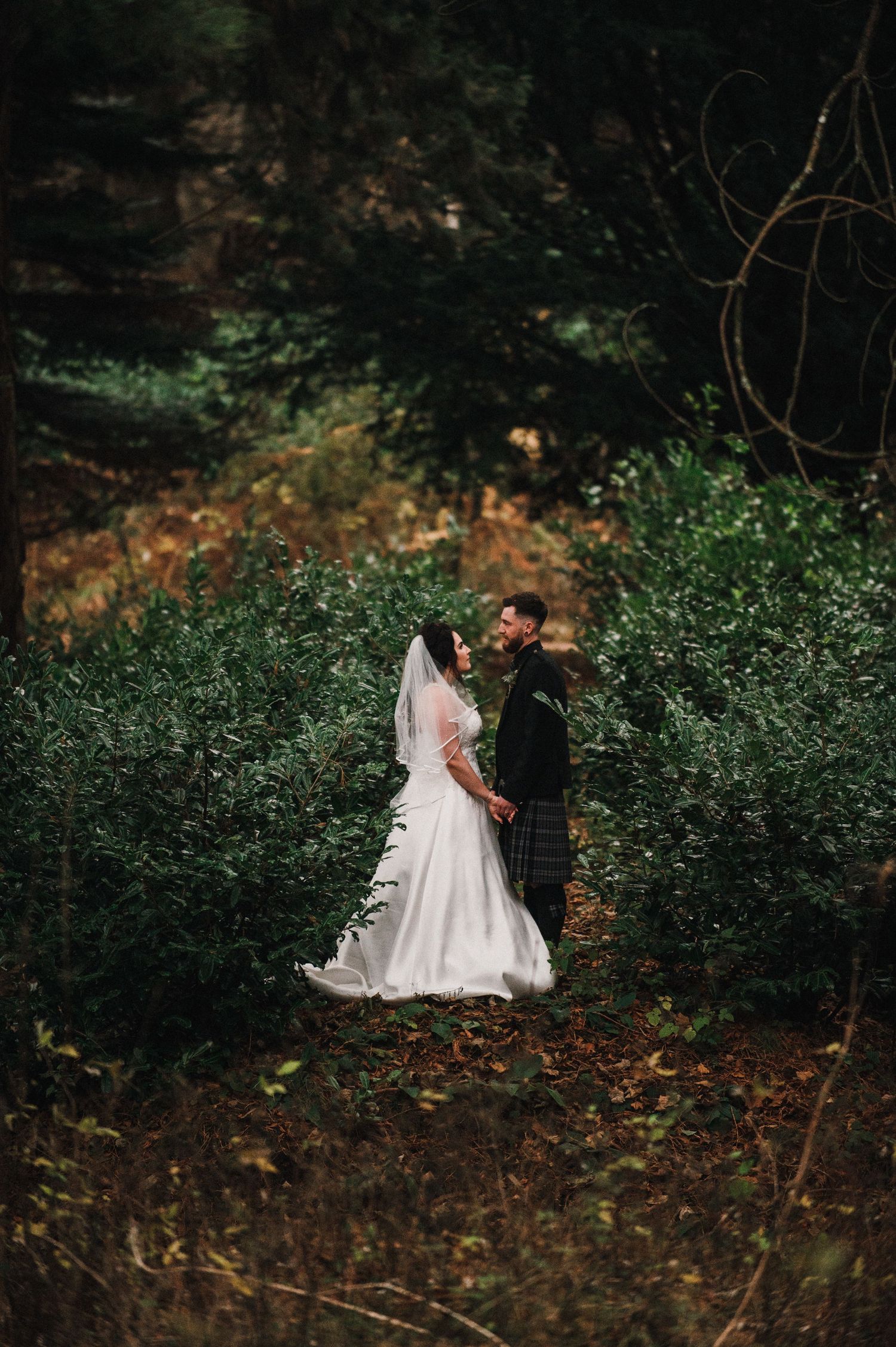 Wedding portrait set among lush greenery and fallen autumn leaves in a woodland setting.