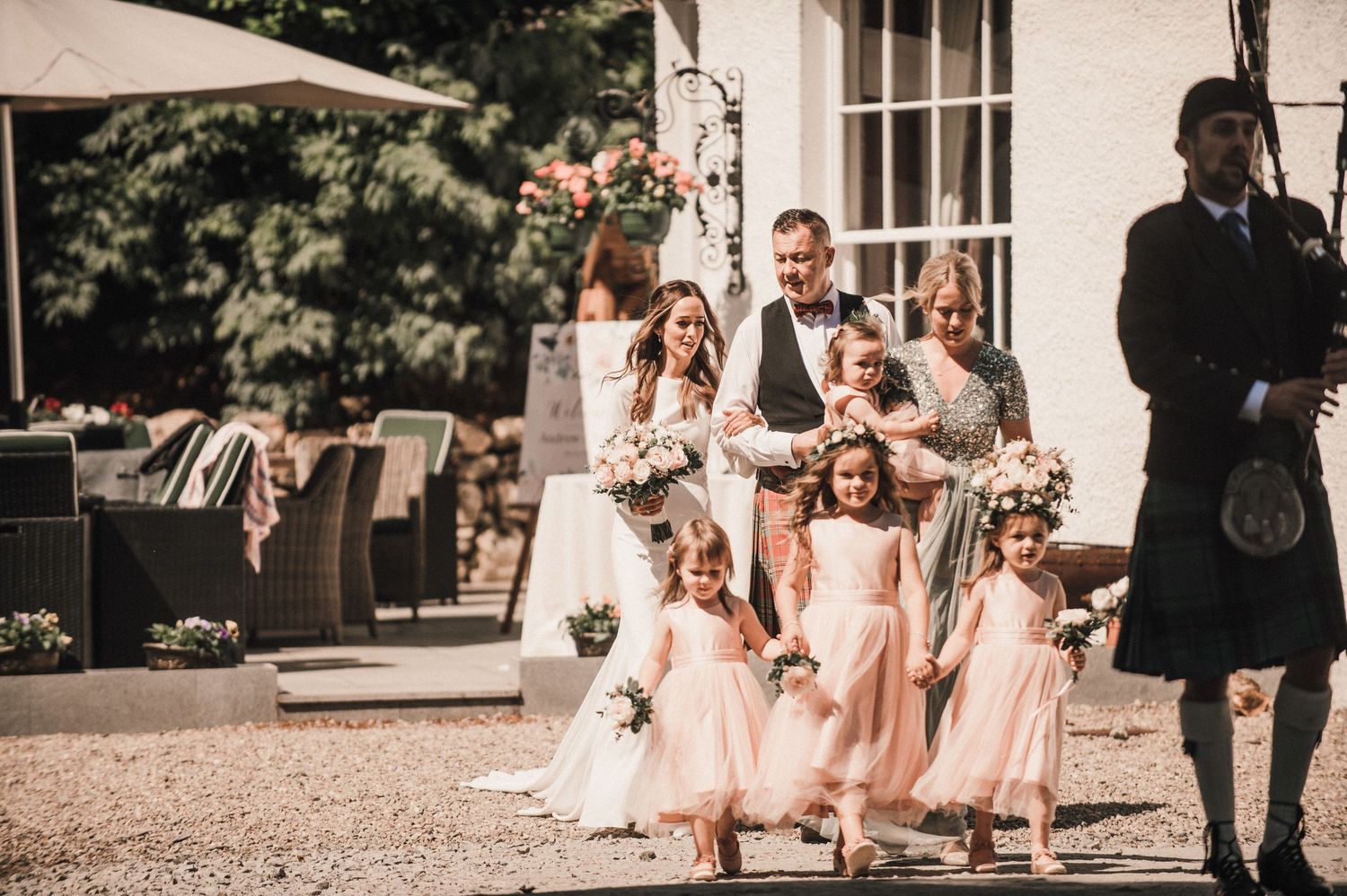 Young bridesmaids in pink dresses follow a bride outside a traditional building.