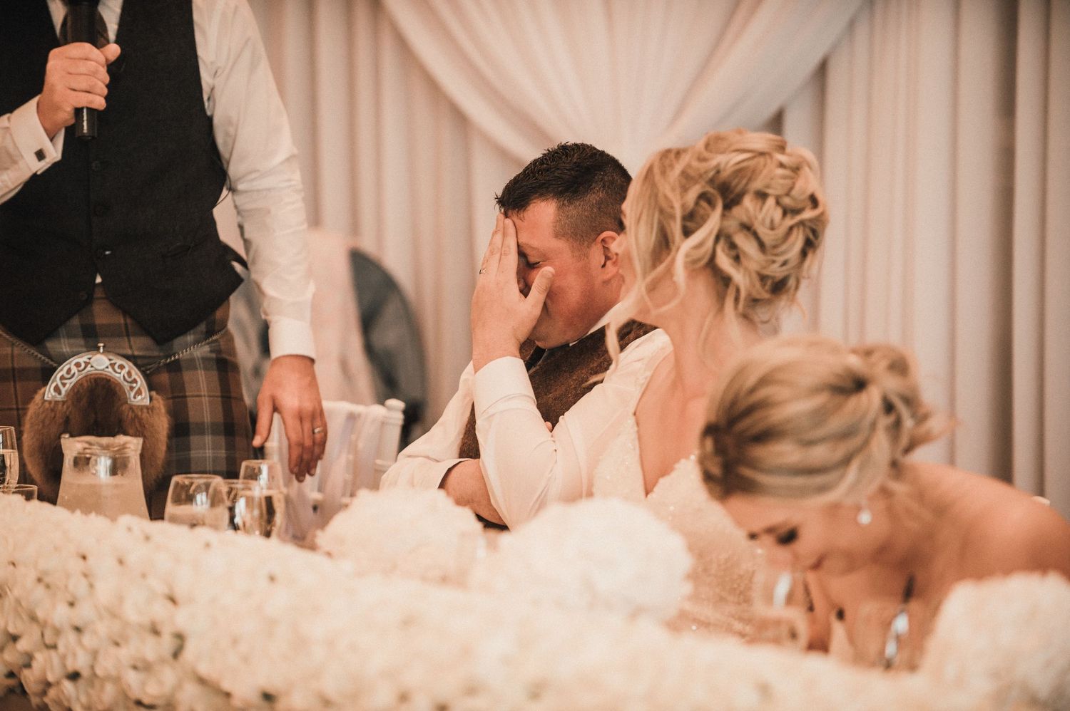 Emotional reactions during wedding speeches at elegant reception with white drape decor.