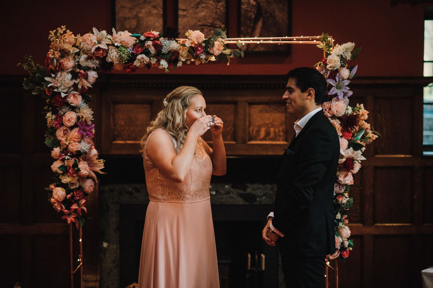 An emotional wedding ceremony moment captured under an arch adorned with pink and white flowers.