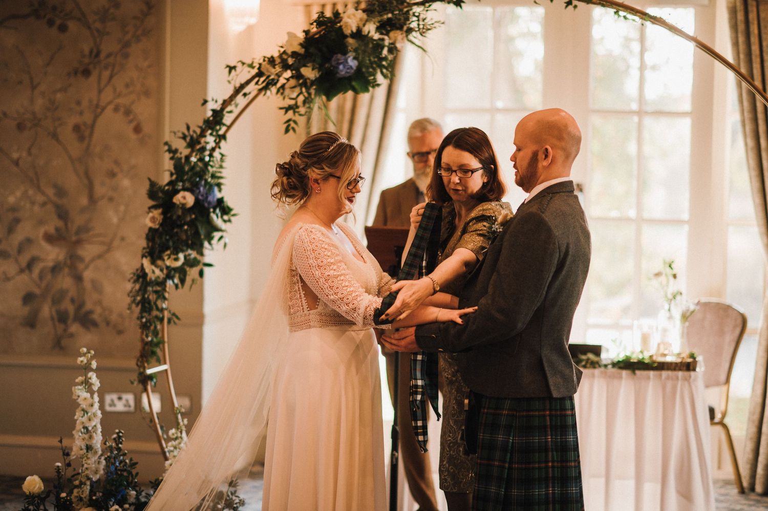 Intimate wedding ceremony under a floral arch decorated with greenery and white flowers.