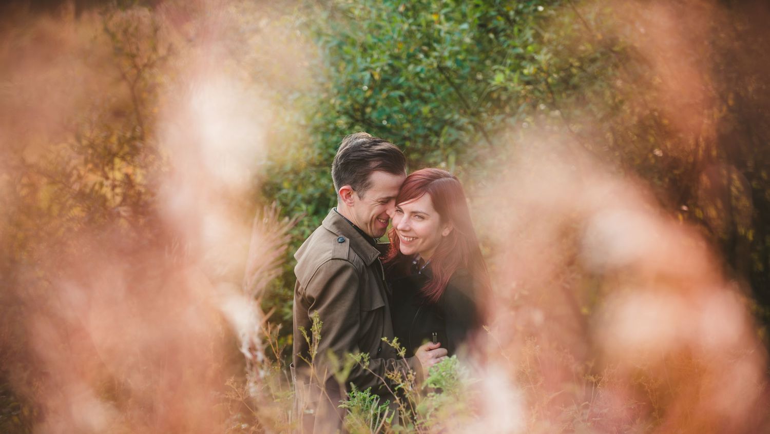A dreamy romantic moment captured through blurred foliage in soft lighting.
