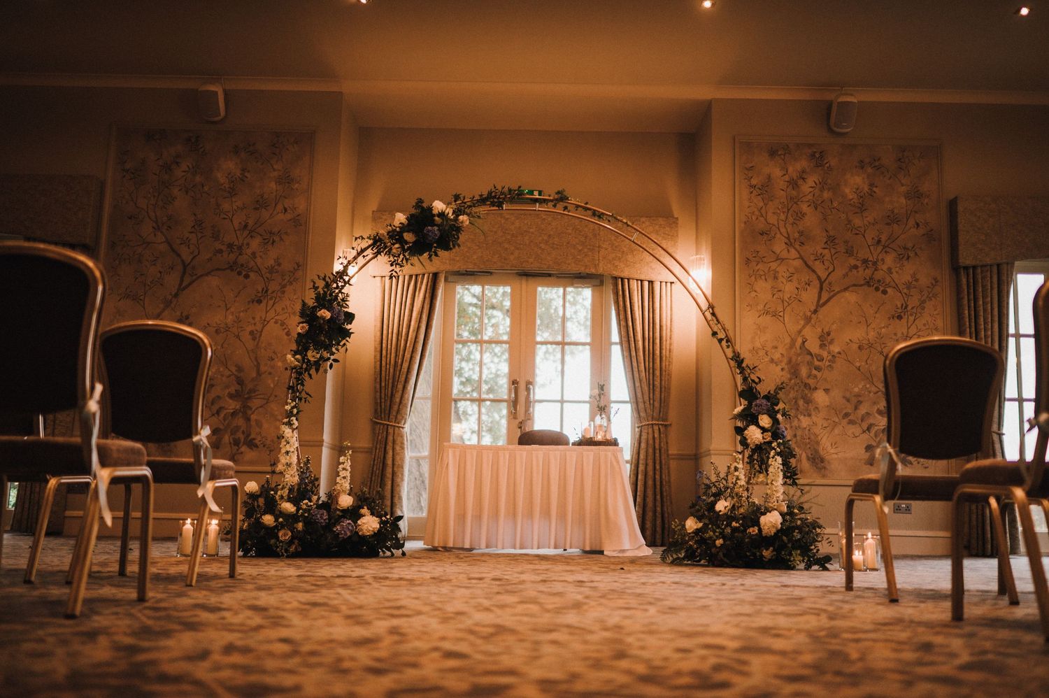 Wedding ceremony arch decorated with white fabric and floral arrangements in an elegant room.