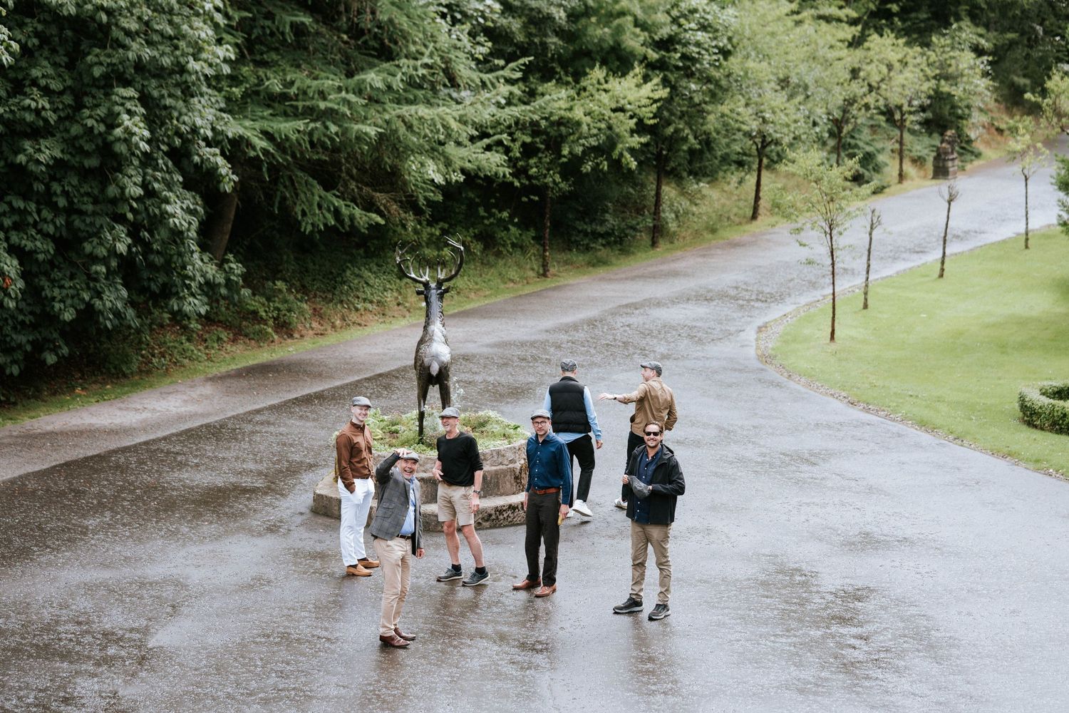 Wedding party walking down a tree-lined path in a park on a rainy day.