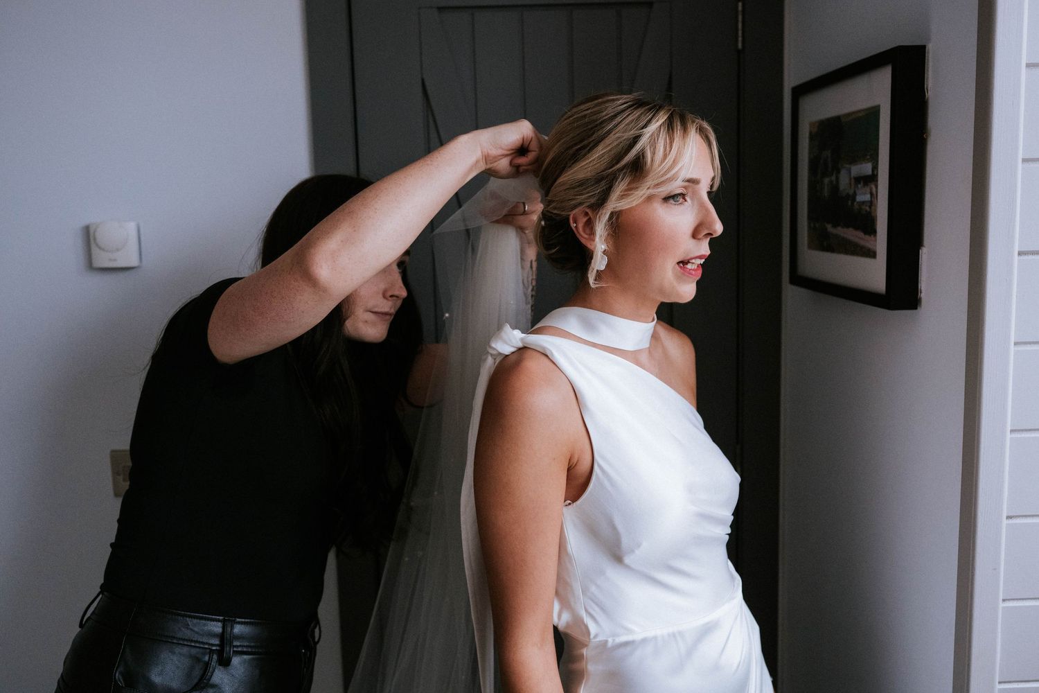 Wedding preparation scene with dress fitting in dimly lit room.