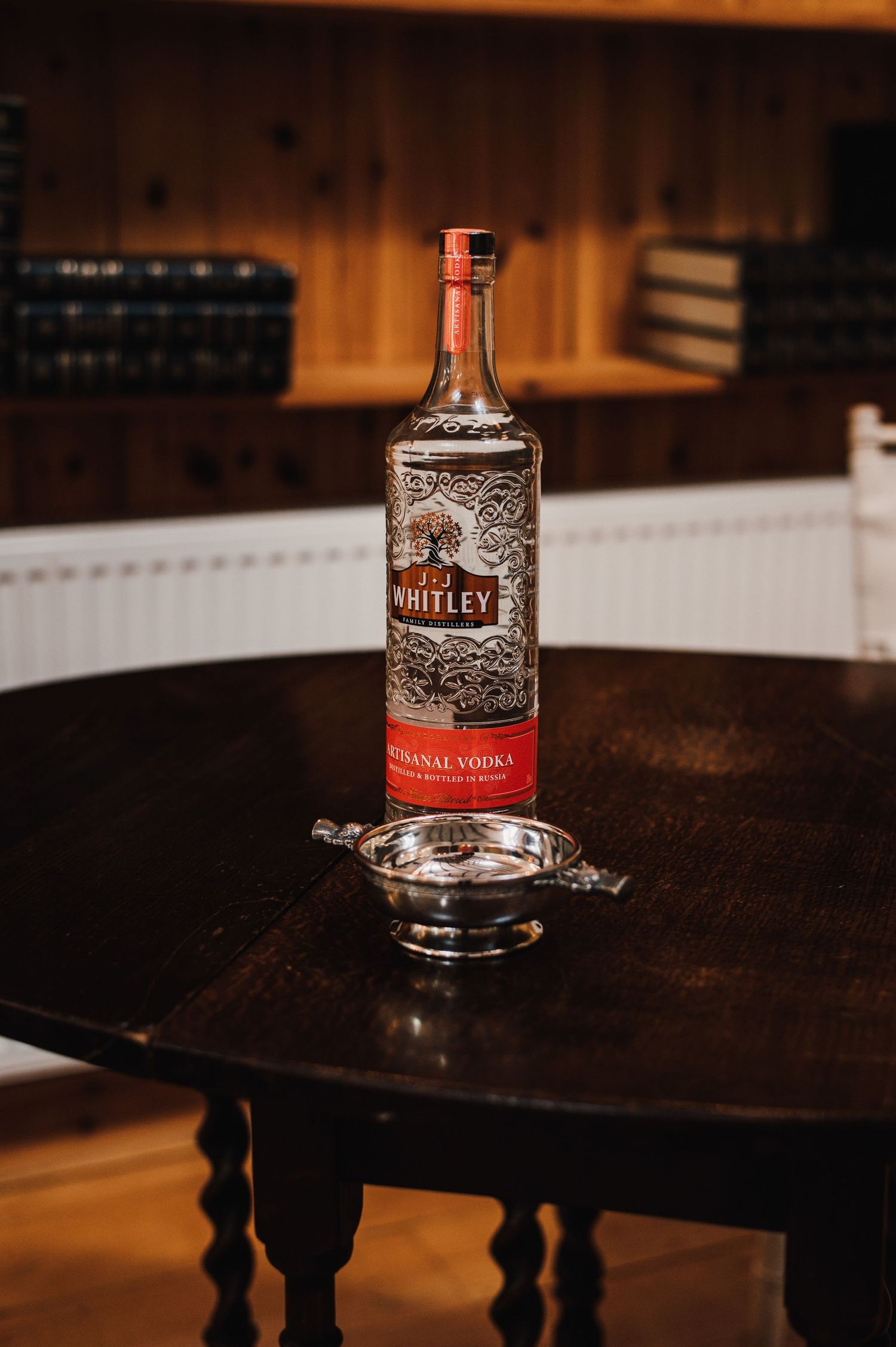 A bottle of JH Whitley whiskey sits on a dark wooden table in warm lighting.