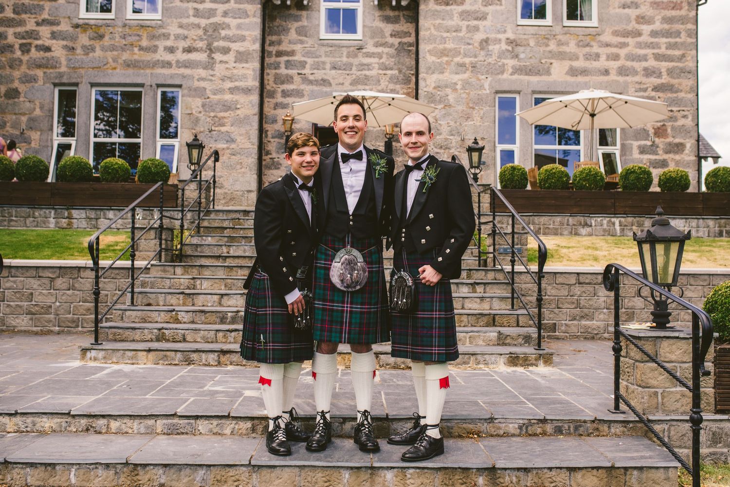 A row of guests in formal attire standing on stone steps outside a brick building at a special event.