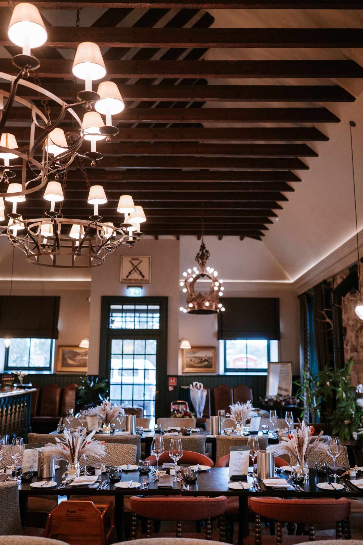Elegant reception venue with exposed wooden beams and chandeliers set for a wedding celebration.