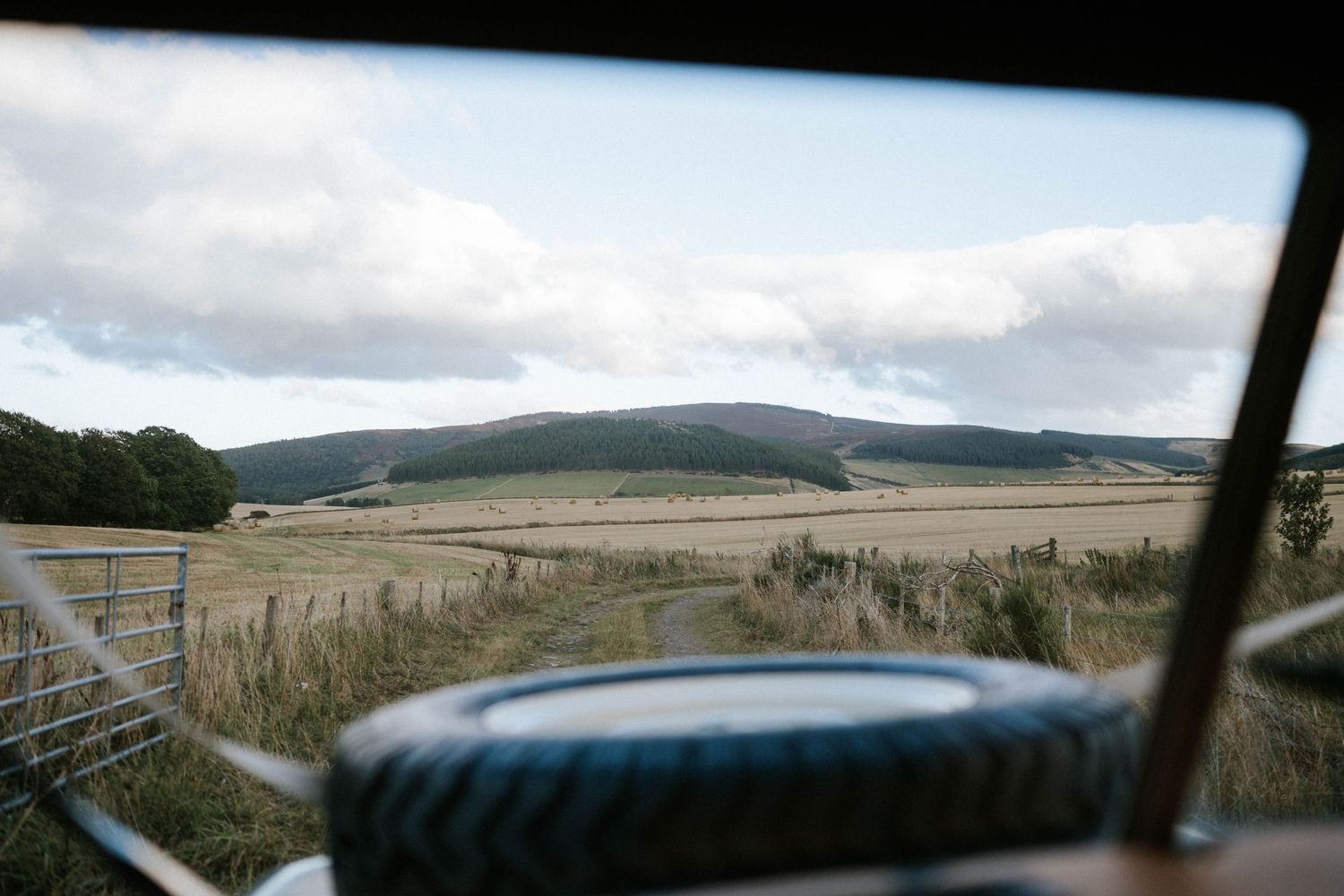 View through a car window of rolling hills and countryside under cloudy skies.