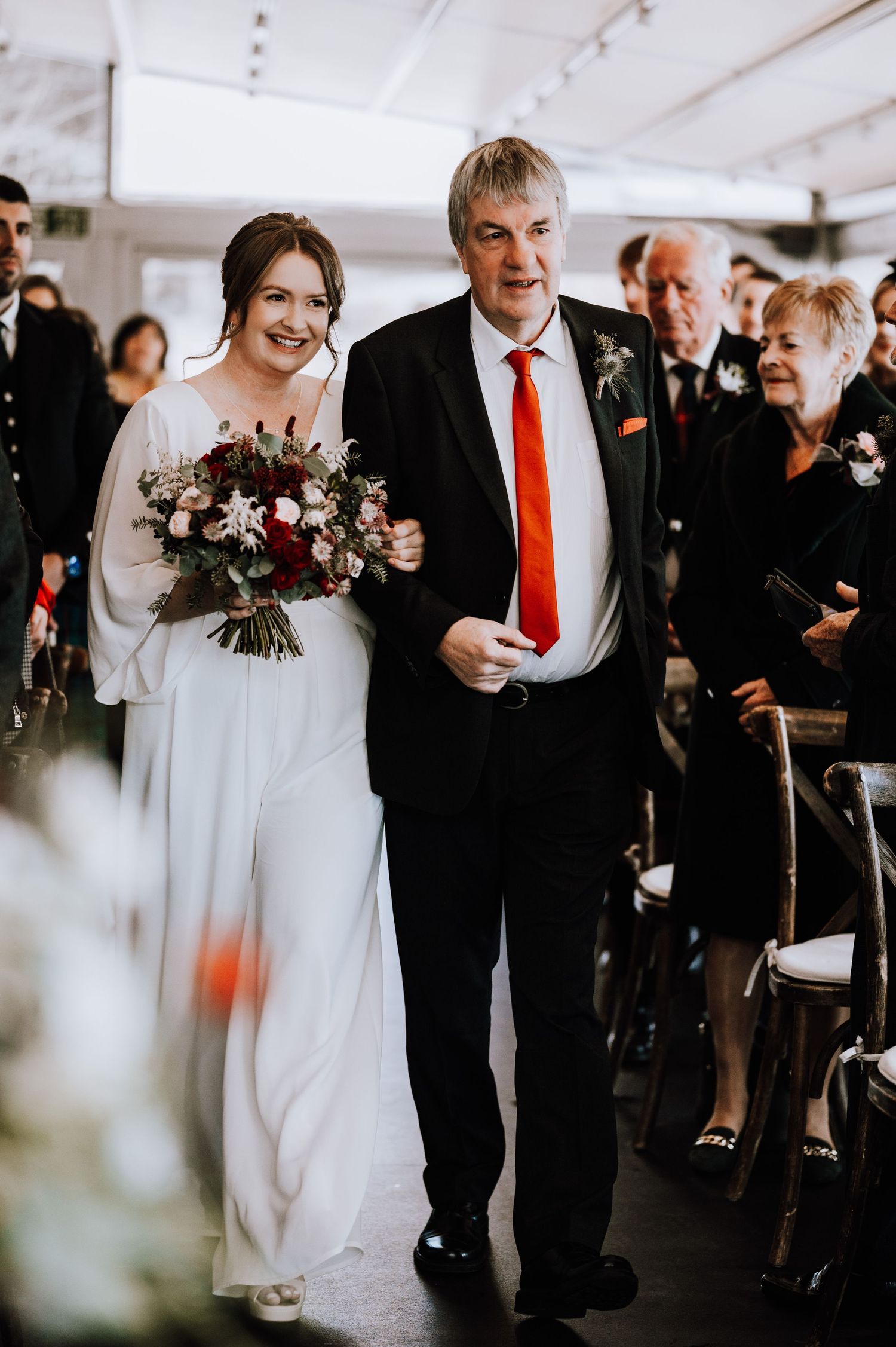 Same Sex Wedding Photography. Wedding procession walks down aisle under white tent with guests looking on.