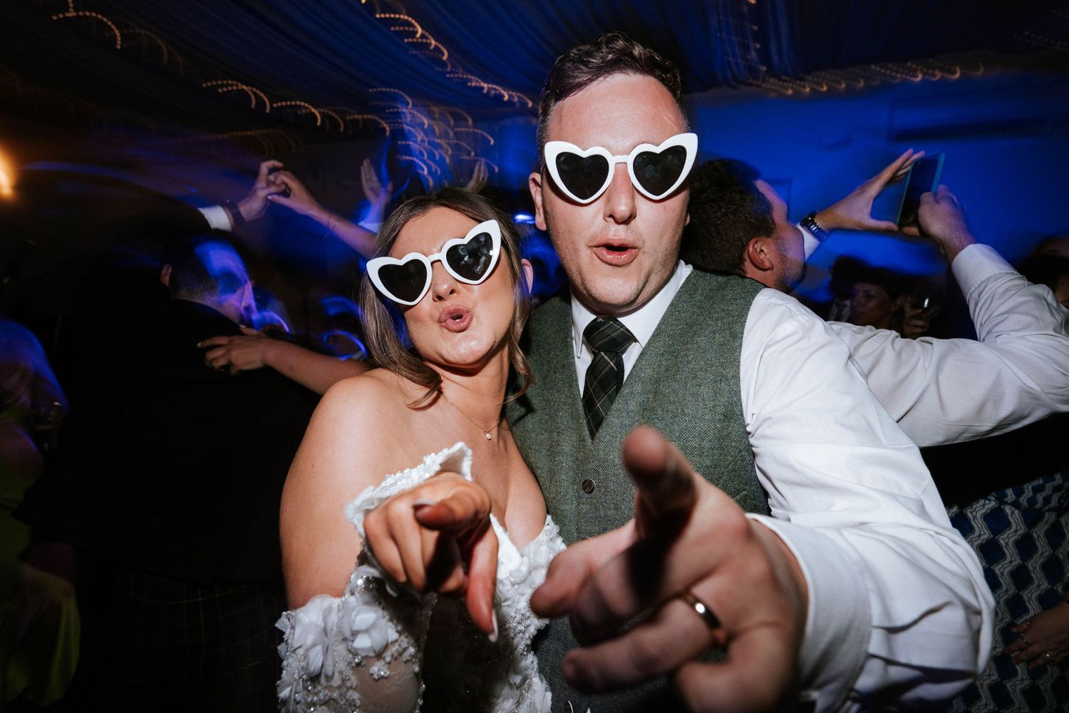 Aberdeen Wedding Photography. Wedding party dancing and celebrating at a lively reception with blue lighting and sunglasses.