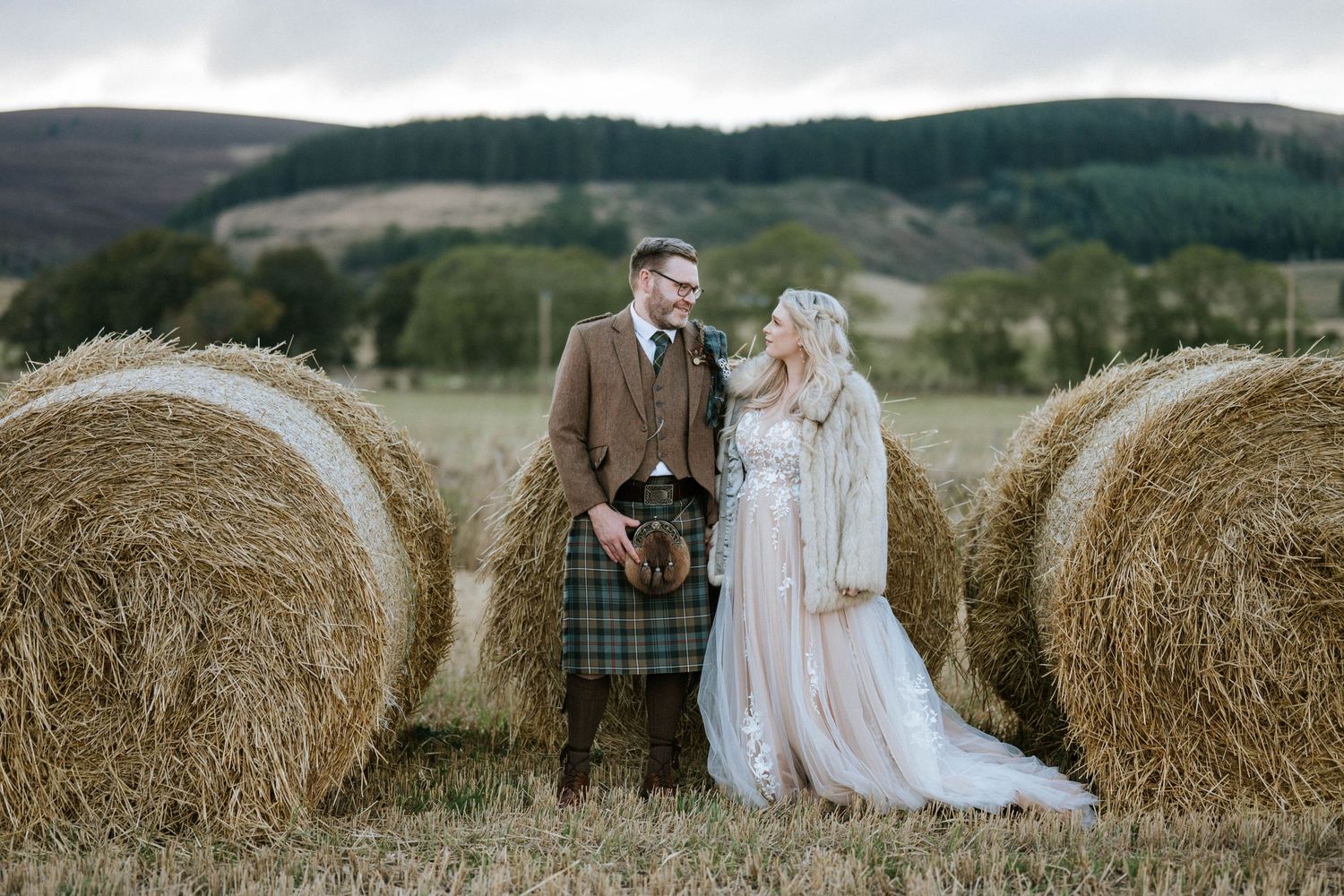 A romantic wedding photo session with hay bales in a rustic countryside setting.