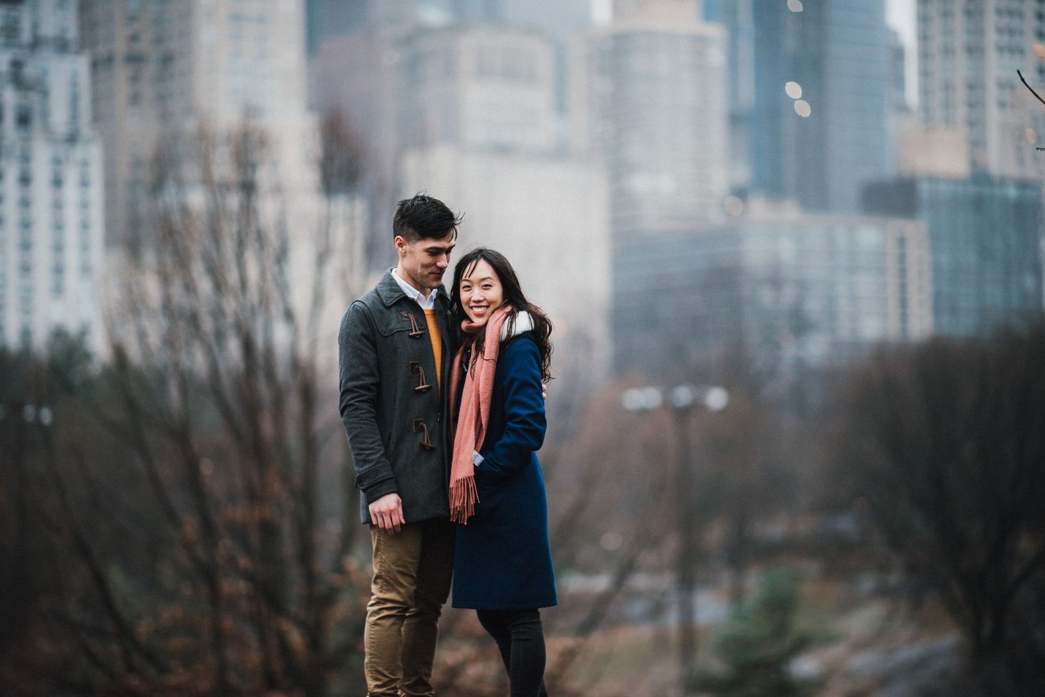 A couple shares a romantic moment in front of a city skyline on a foggy winter day.