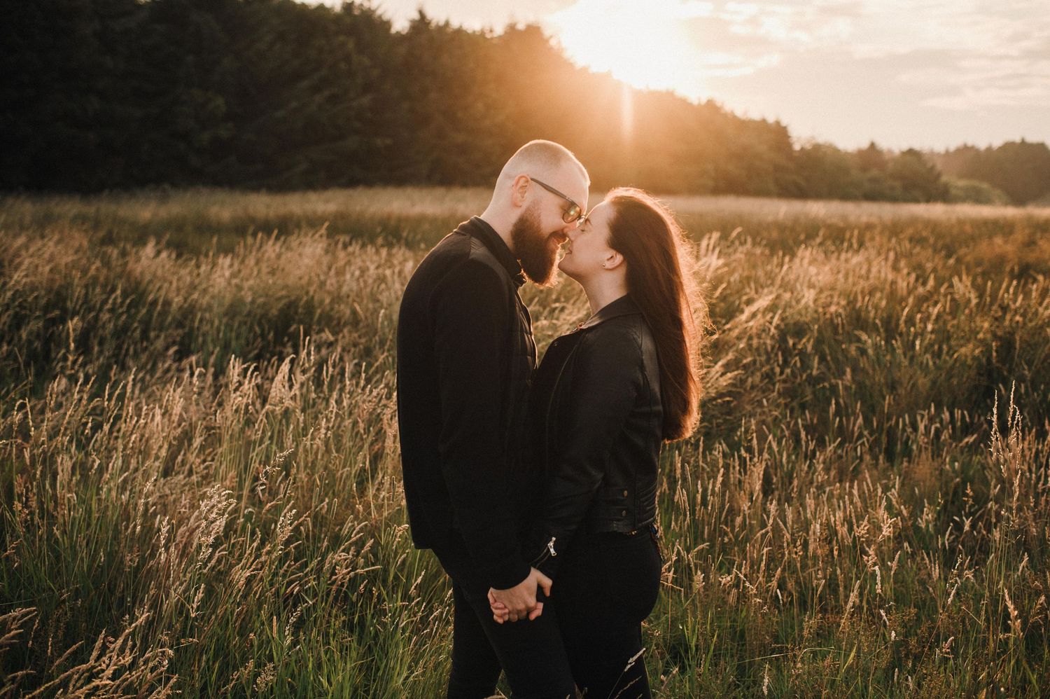 Romantic couple embraces in sunlit field during golden hour engagement photography session.