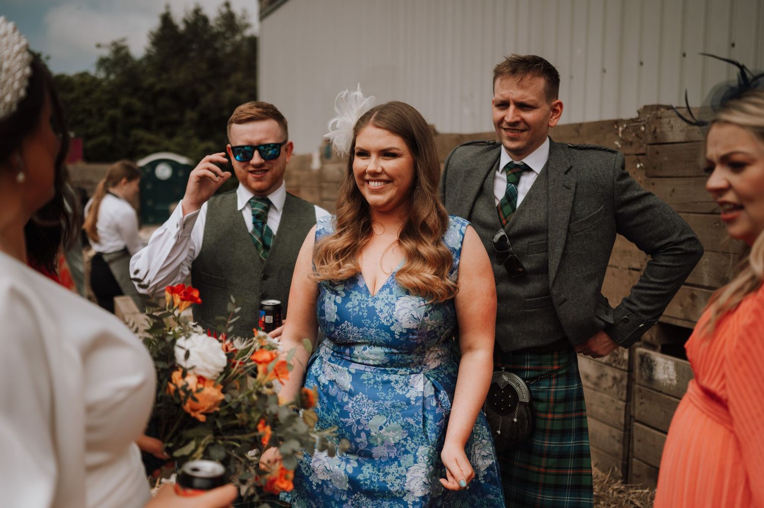 Wedding guests in kilts and formal attire gather outdoors for summer celebrations.