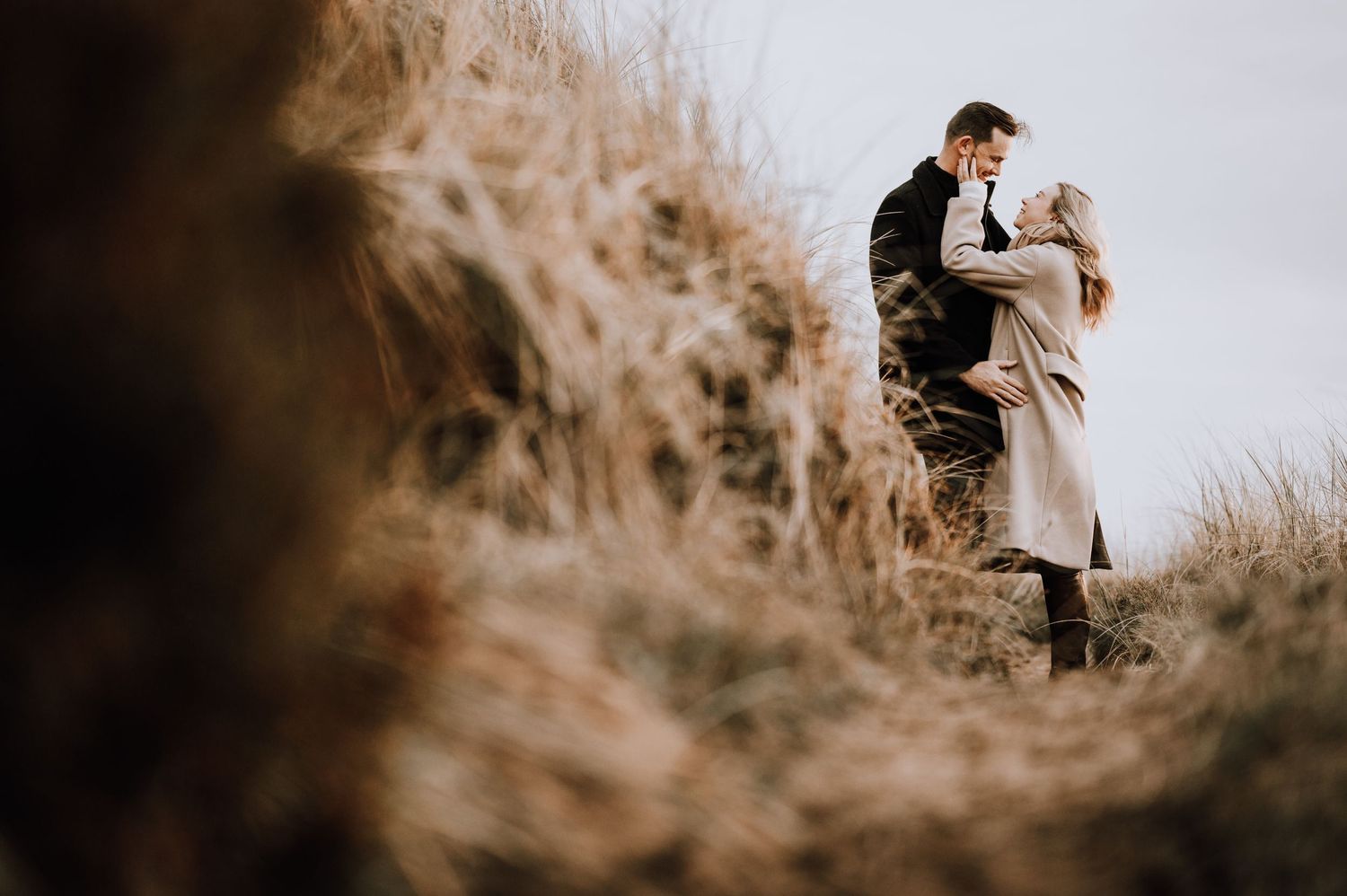 Couple embraces on dramatic coastal cliff path during golden hour.
