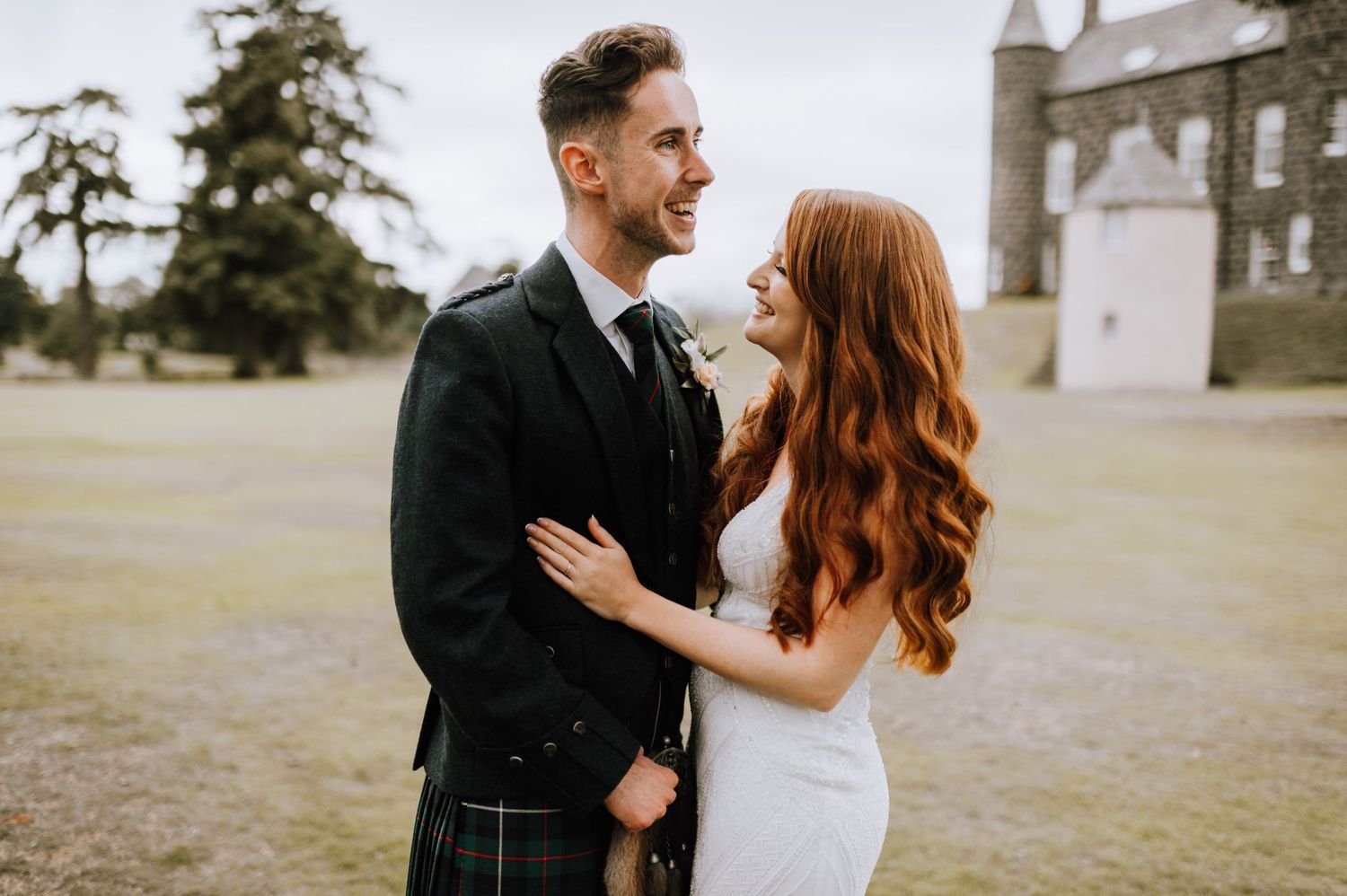 A couple embraces during their Scottish wedding with a castle in the background.