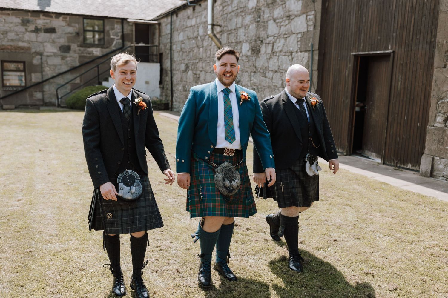 Three men walking together while wearing traditional Scottish kilts and formal attire.