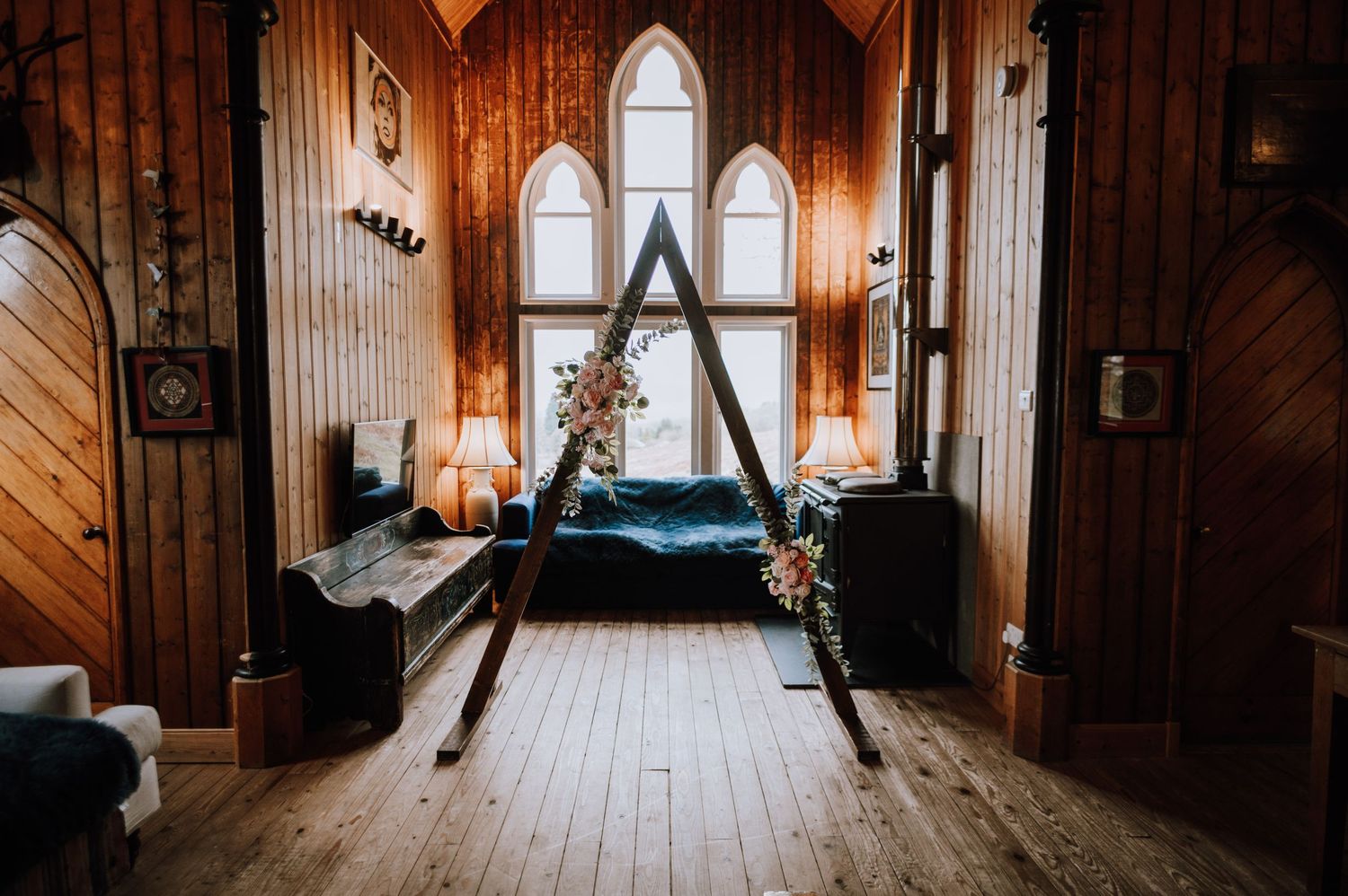 Rustic wooden chapel interior with A-frame windows and natural light streaming in.