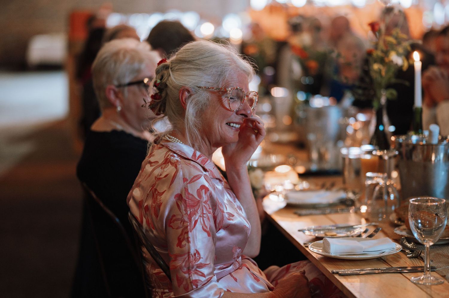 Wedding guests listen attentively during reception dinner in brick-walled venue.
