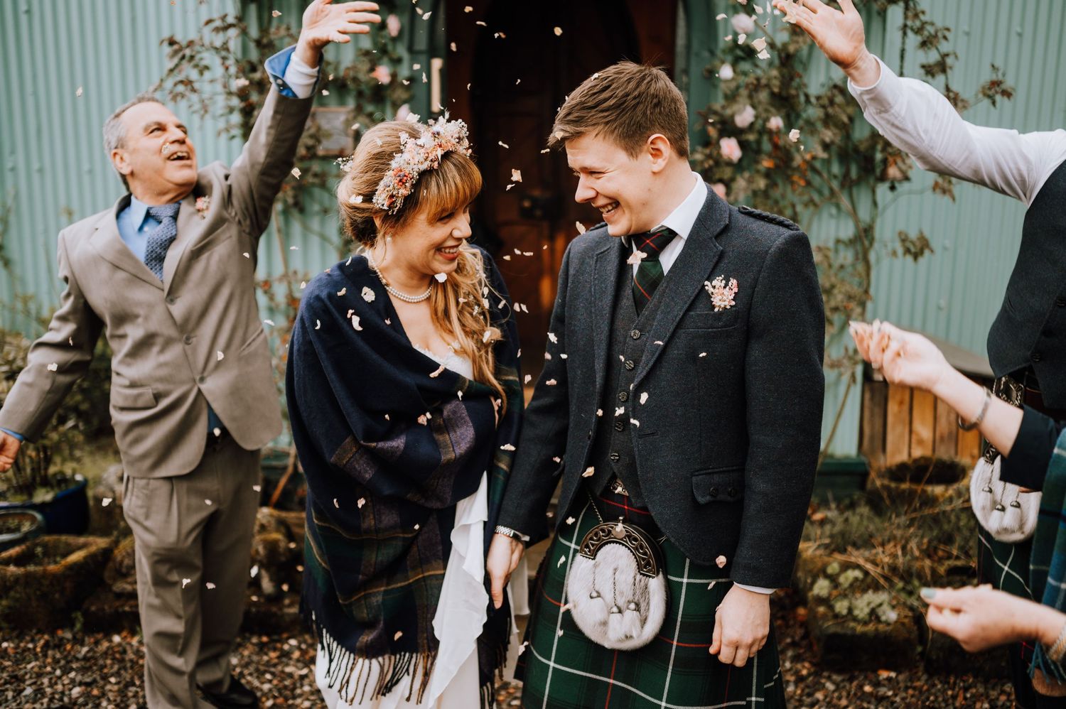 Guests throw confetti during outdoor Scottish wedding celebration.