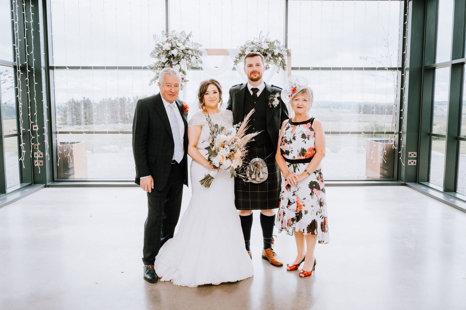 Small wedding group portrait with Scottish kilt and formal attire in bright indoor setting.