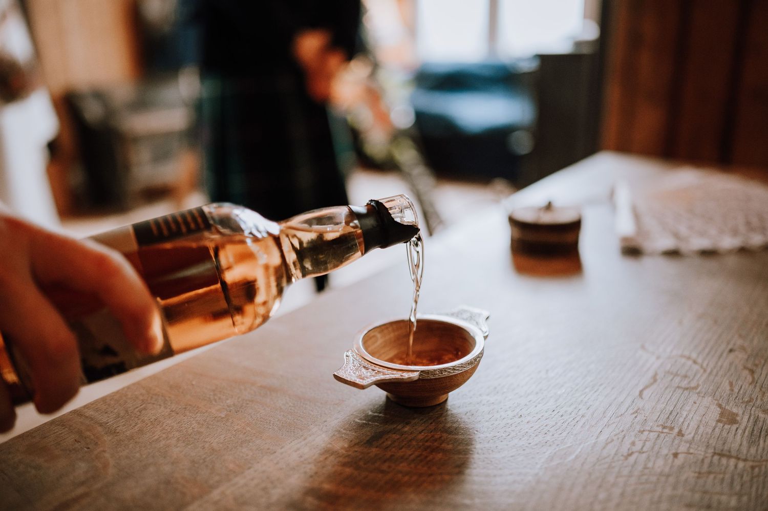 Liquid being poured from a bottle into a small glass cup on a wooden table.