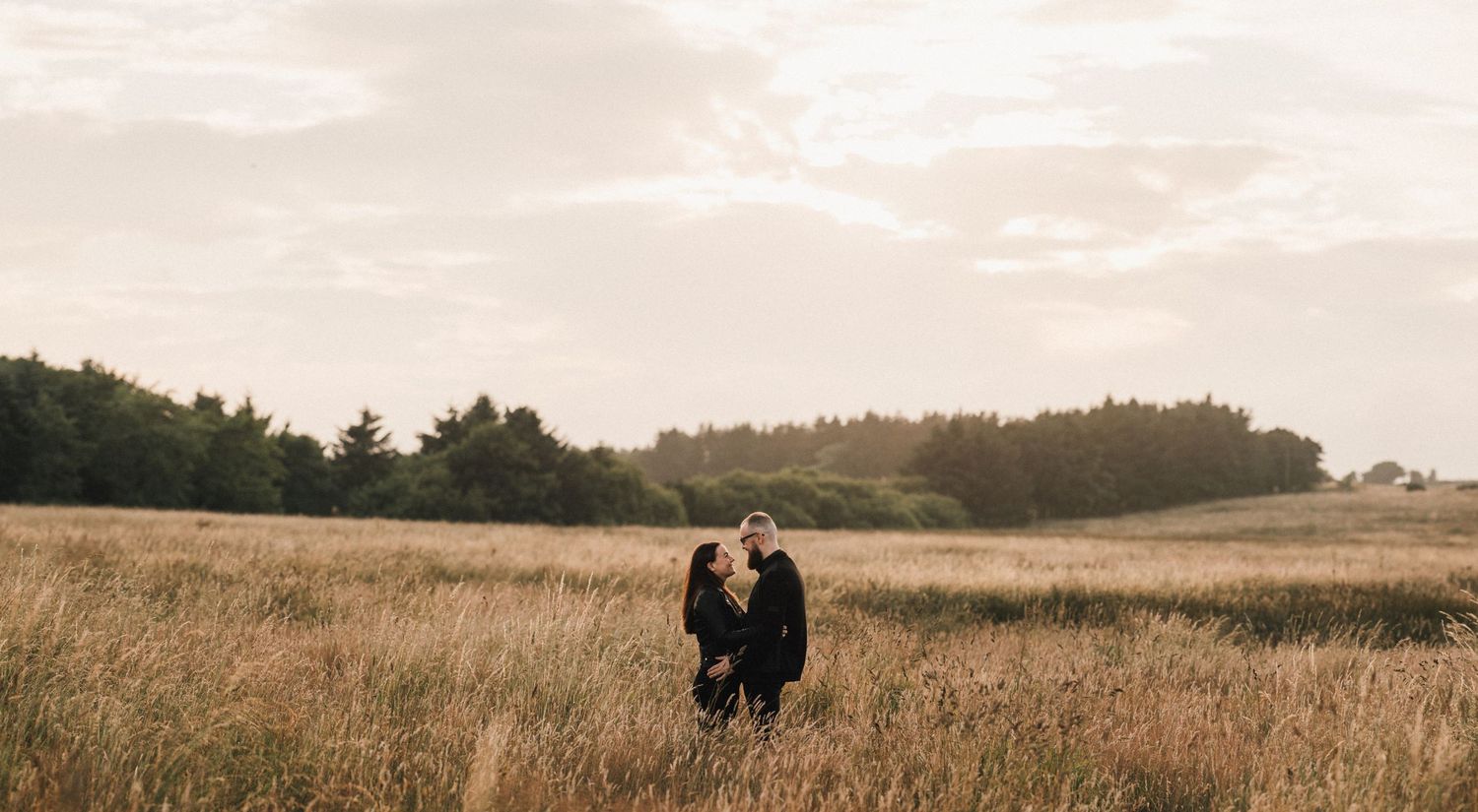 Two figures embracing in a scenic field with trees silhouetted against the evening sky.